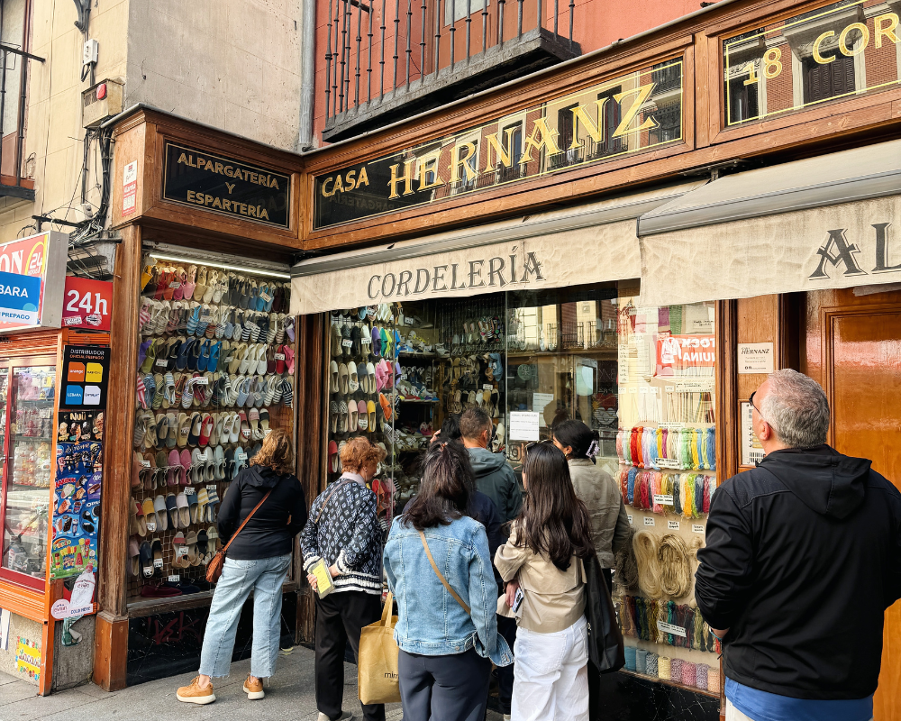  The shopfront of Casa Hernanz covered in colourful espadrilles, with a crowd gathered outside. 