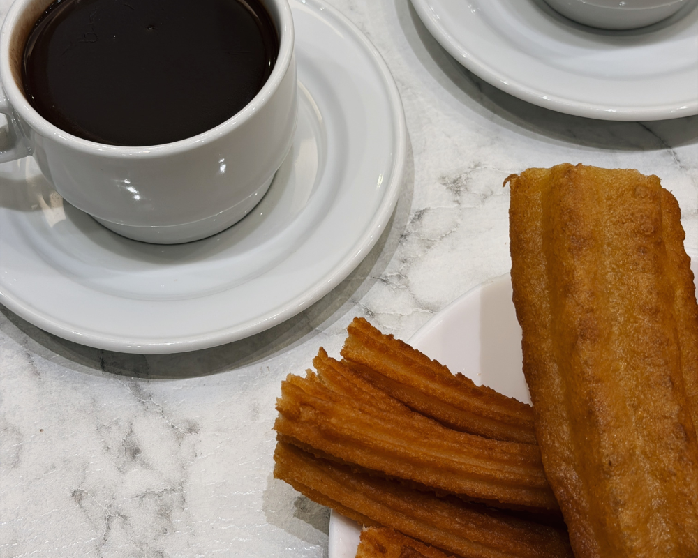  Thick golden churros and a cup of dark molten chocolate on a marble table at Chocolatería San Ginés. 