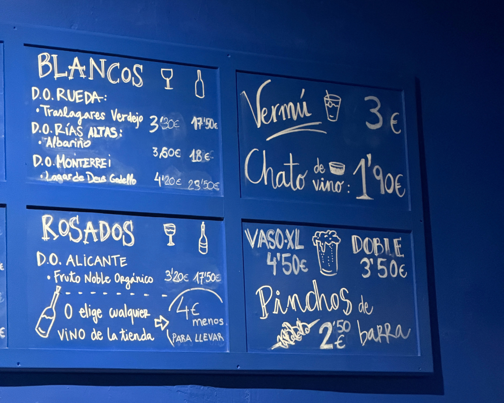  A bright blue chalkboard menu listing vermút, wines and pinchos at a Madrid bar. 