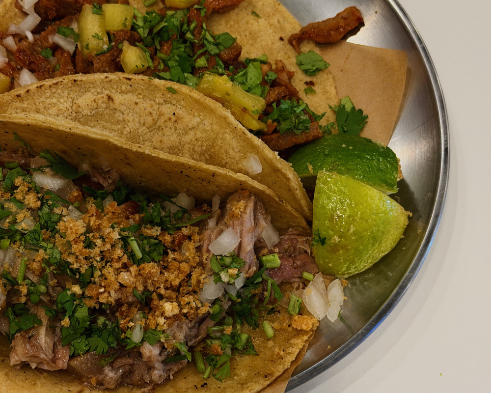  Two corn tortilla tacos with pulled pork and al pastor, garnished with coriander, onion and lime at Puerco Taqueria Madrid. 