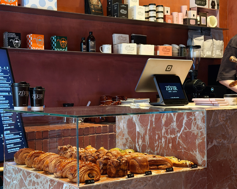  The marble counter at Zéfir café lined with croissants and pastries, with branded takeaway cups and coffee products behind. 