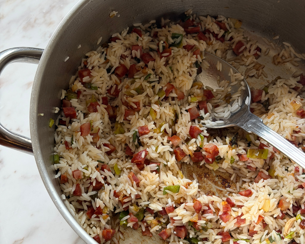  Short grain rice being toasted with chorizo and spring onions in a steel pot 