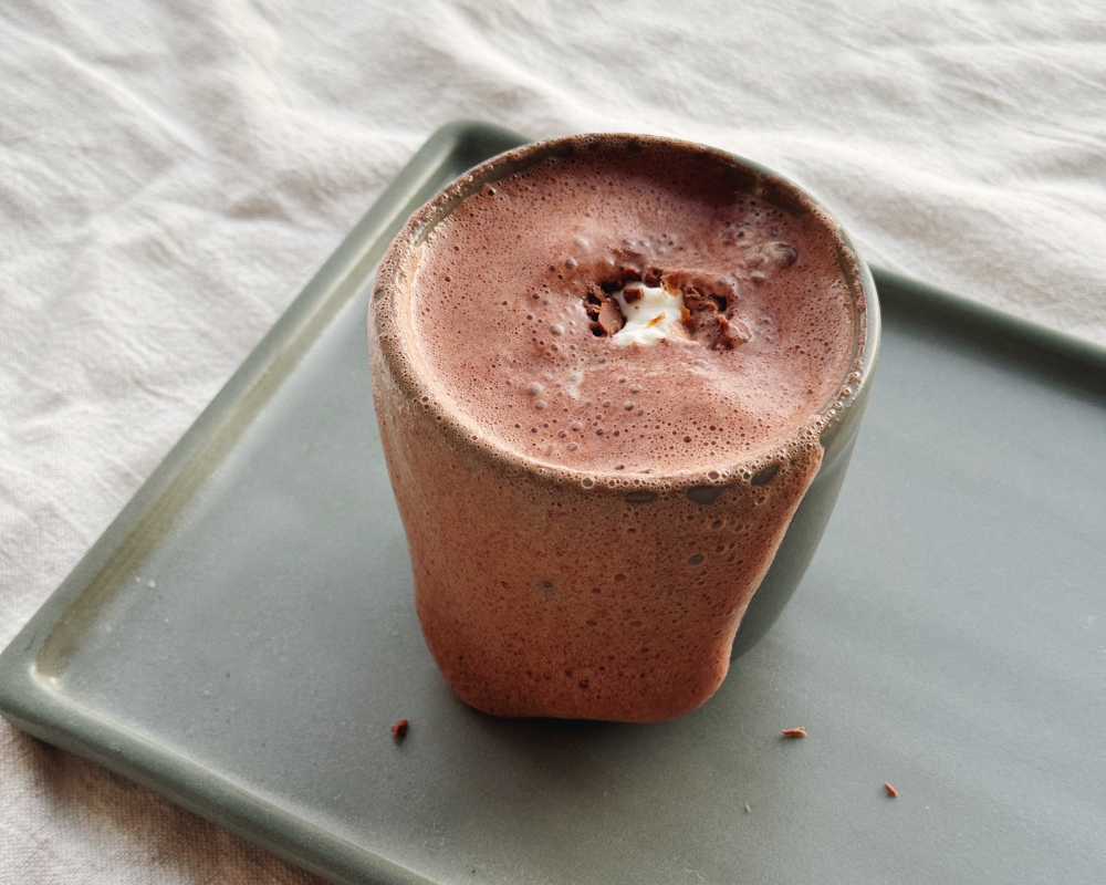  Warm, frothy Chai Hot Chocolate overflowing over a grey cup 