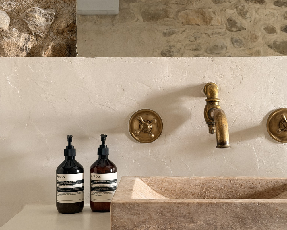  Stone bathroom sink with brass fittings against a rustic stone wall at Maison Santcha 