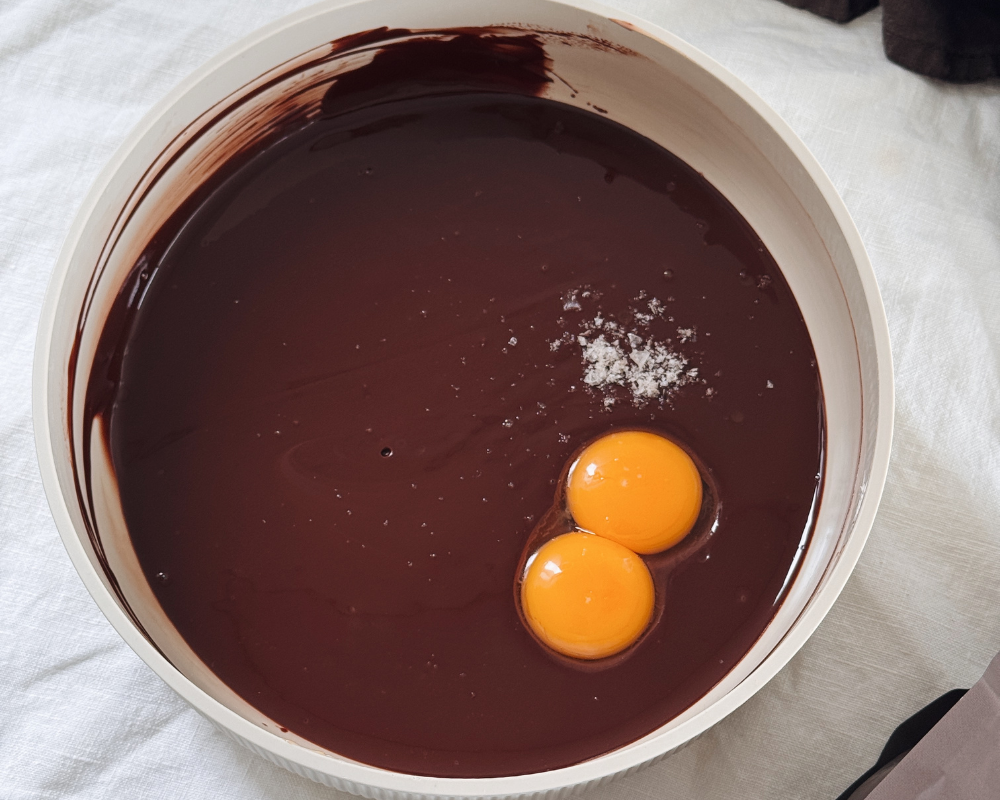   Egg yolks and sea salt added to baked chocolate ganache mixture in a large bowl 