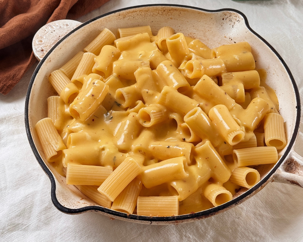  A white skillet pan with rigatoni in a cheesy sauce for truffle mac and cheese 