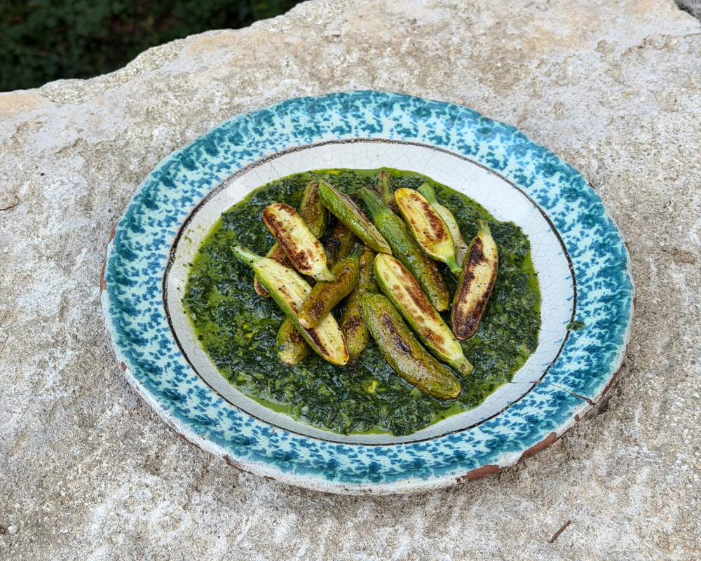  A plate of browned baby zucchini served over pistou, set on a stone ledge. 