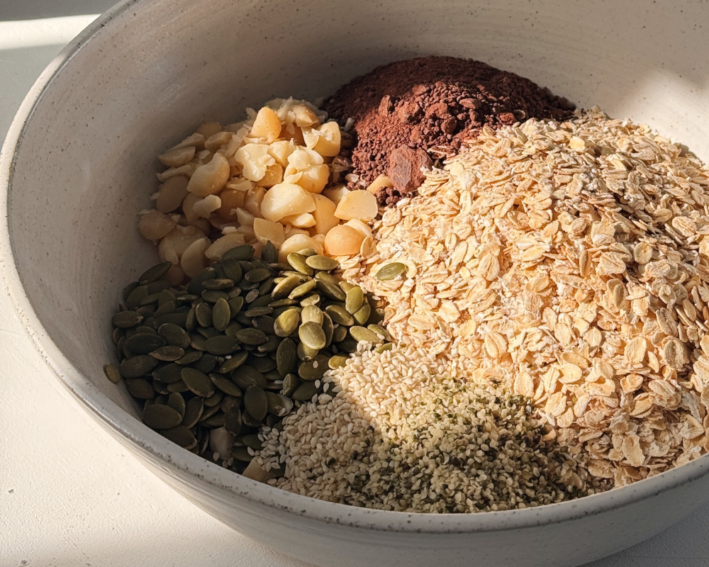  Bowl of chocolate granola ingredients before baking, with oats, macadamias, pepitas, sesame seeds and cocoa powder. 