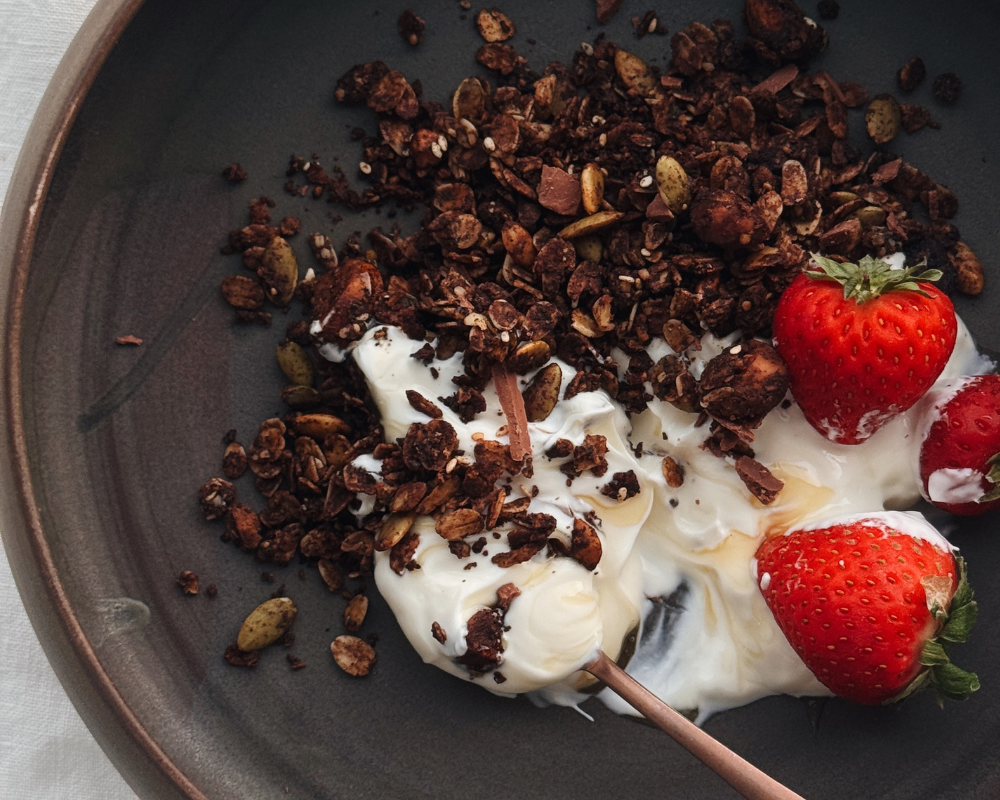  Bowl of chocolate granola served over Greek yoghurt with fresh strawberries and a drizzle of honey. 