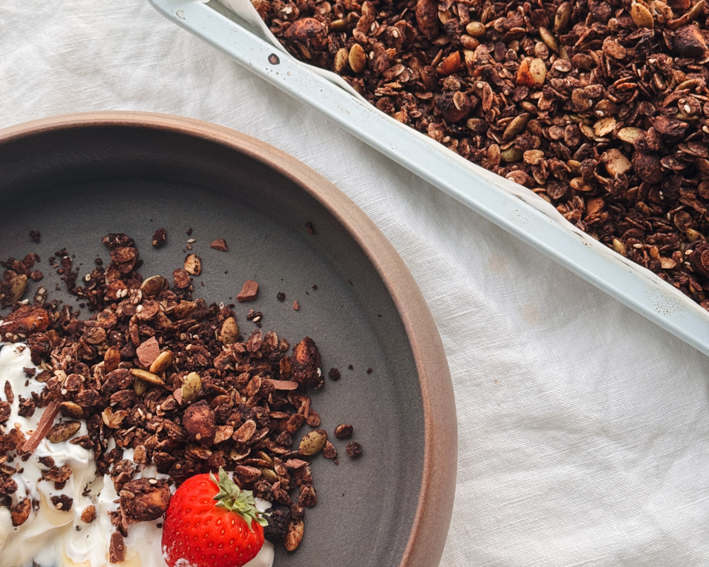  Chocolate granola with strawberries and yoghurt, served beside the baking tray of granola. 