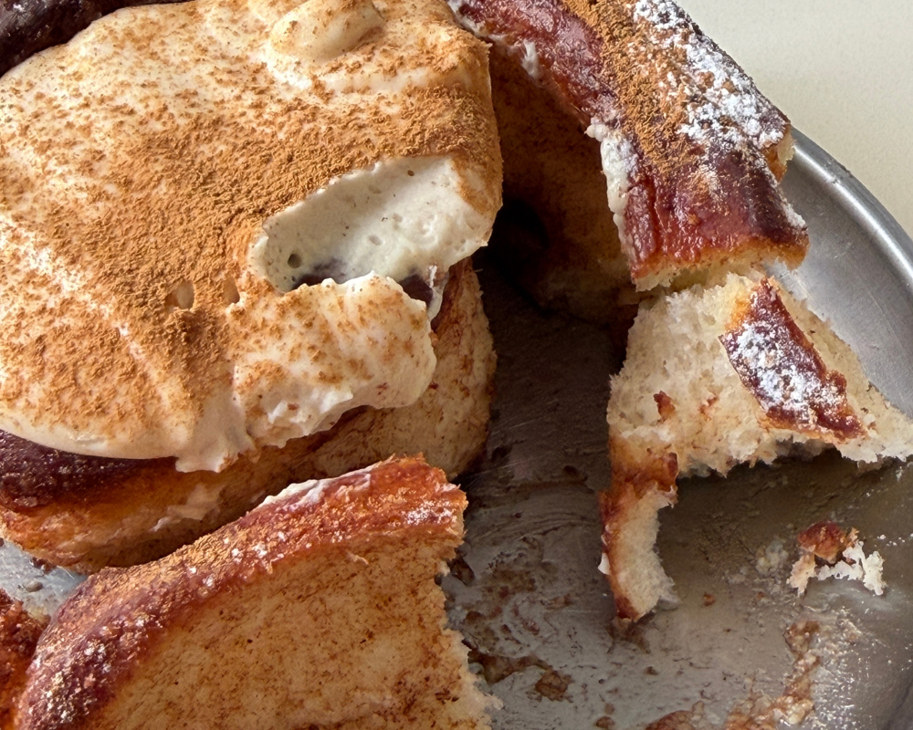  Cinnamon bun dusted with cinnamon and topped with cream, torn open on a metal tray 