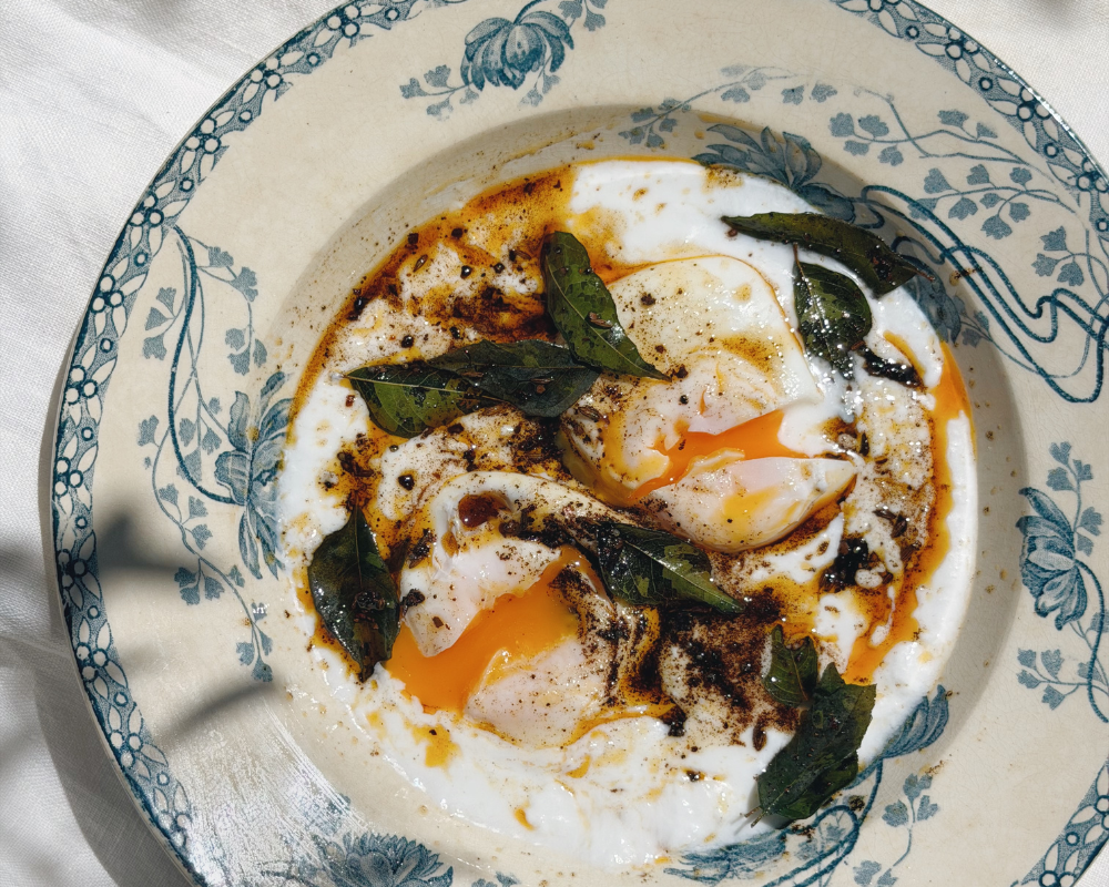  A bowl of poached eggs with the yolk spilling out on a bed of yoghurt topped with spiced ghee for Indian-ish Turkish Eggs 