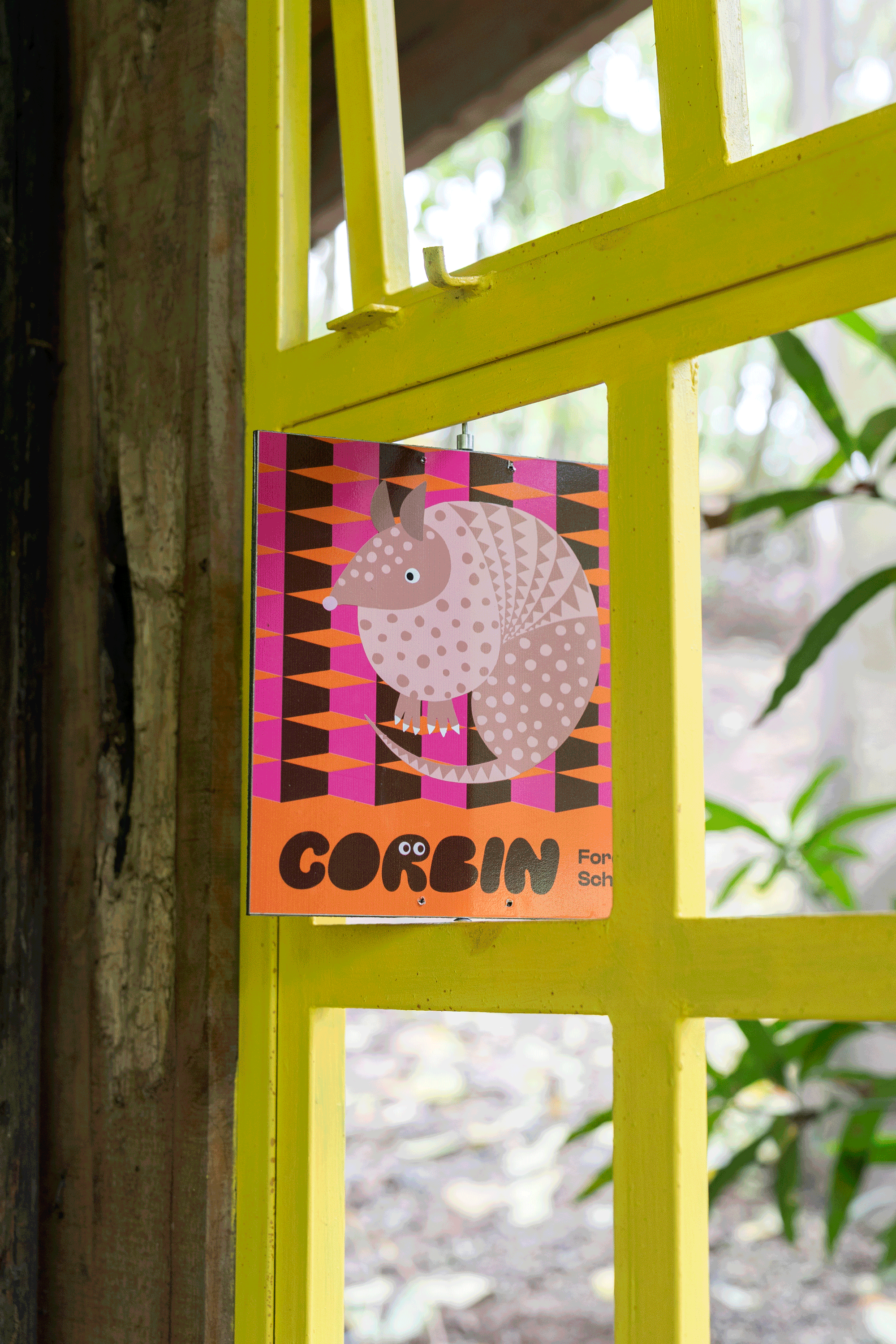 Colorful sign featuring an illustrated animal with a patterned body, sitting on a geometric background, attached to a yellow metal gate.