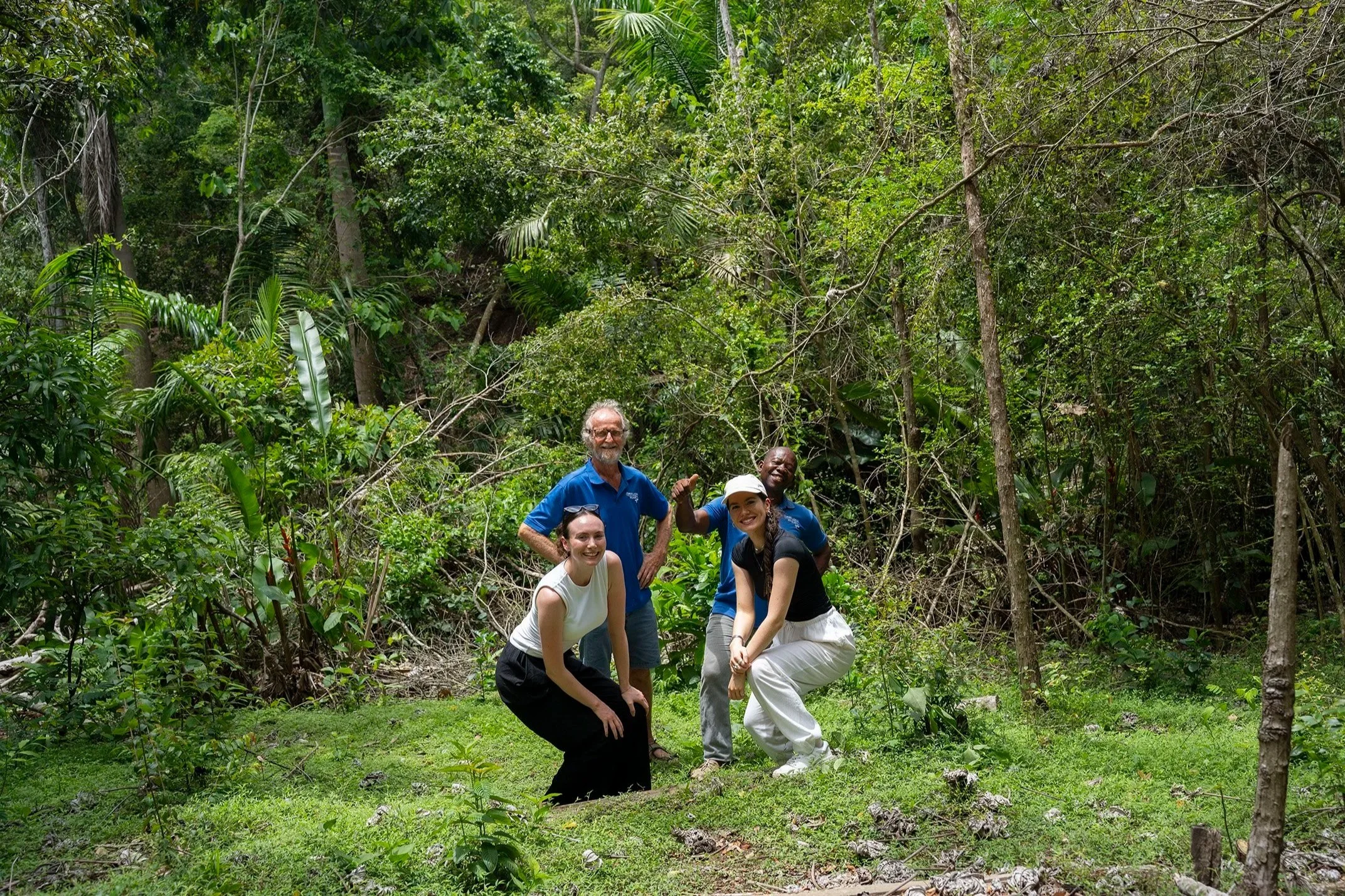 Four people, two women and two men, smiling and posing in a lush green jungle setting.