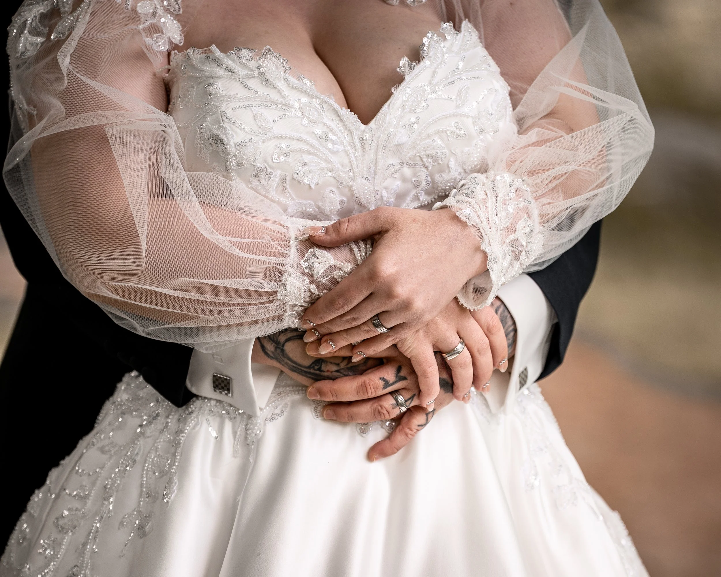 Nahaufnahme eines Brautkleides mit Perlen- und Stickereibeleuchtung, die zu den Schultern und dem Dekolleté führt, während sich die Hände eines Paares um die Taille der Braut legen.