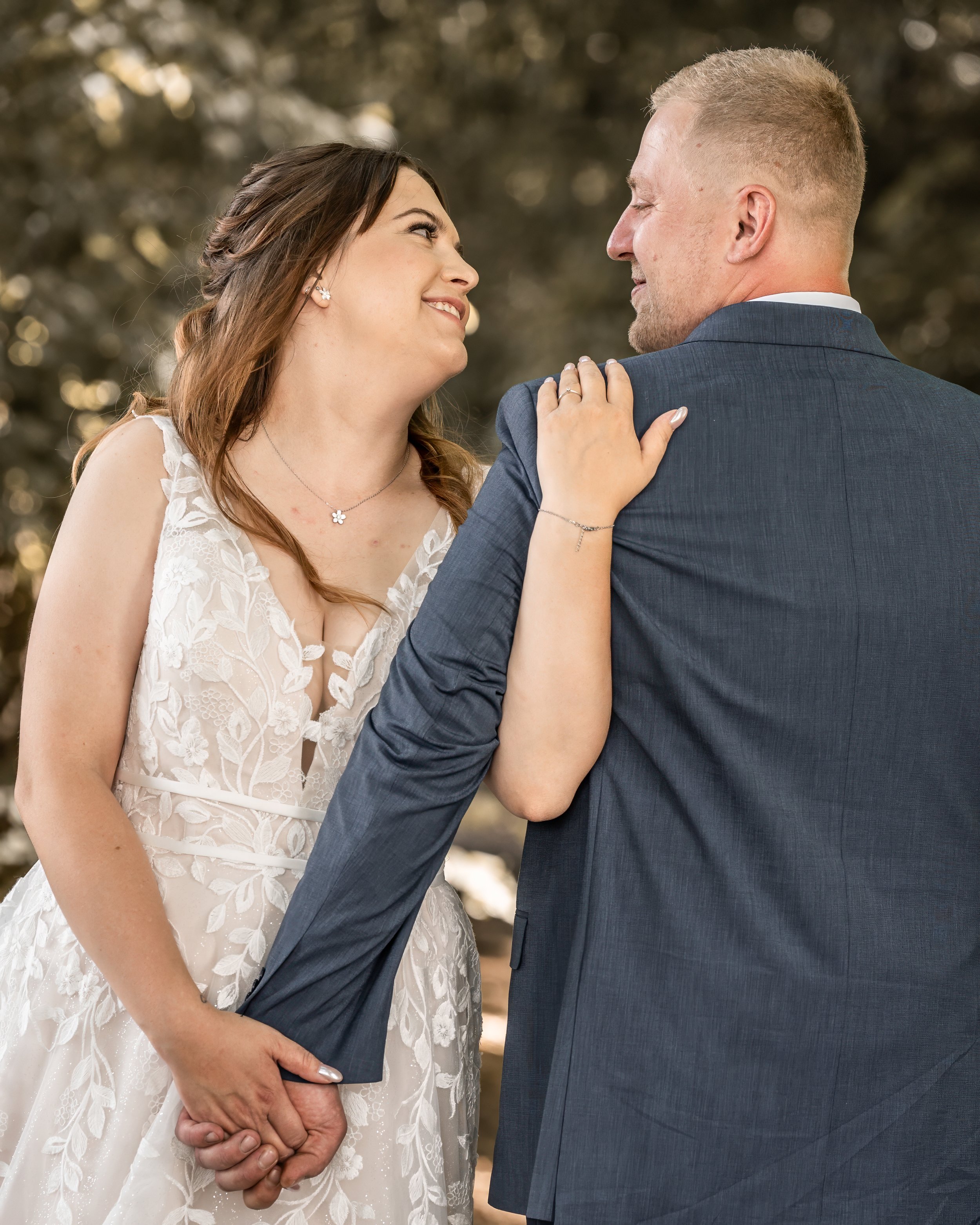Ein Brautpaar, das sich liebevoll ansieht, Händchen hält und sich auf einer Hochzeit im Freien befindet.