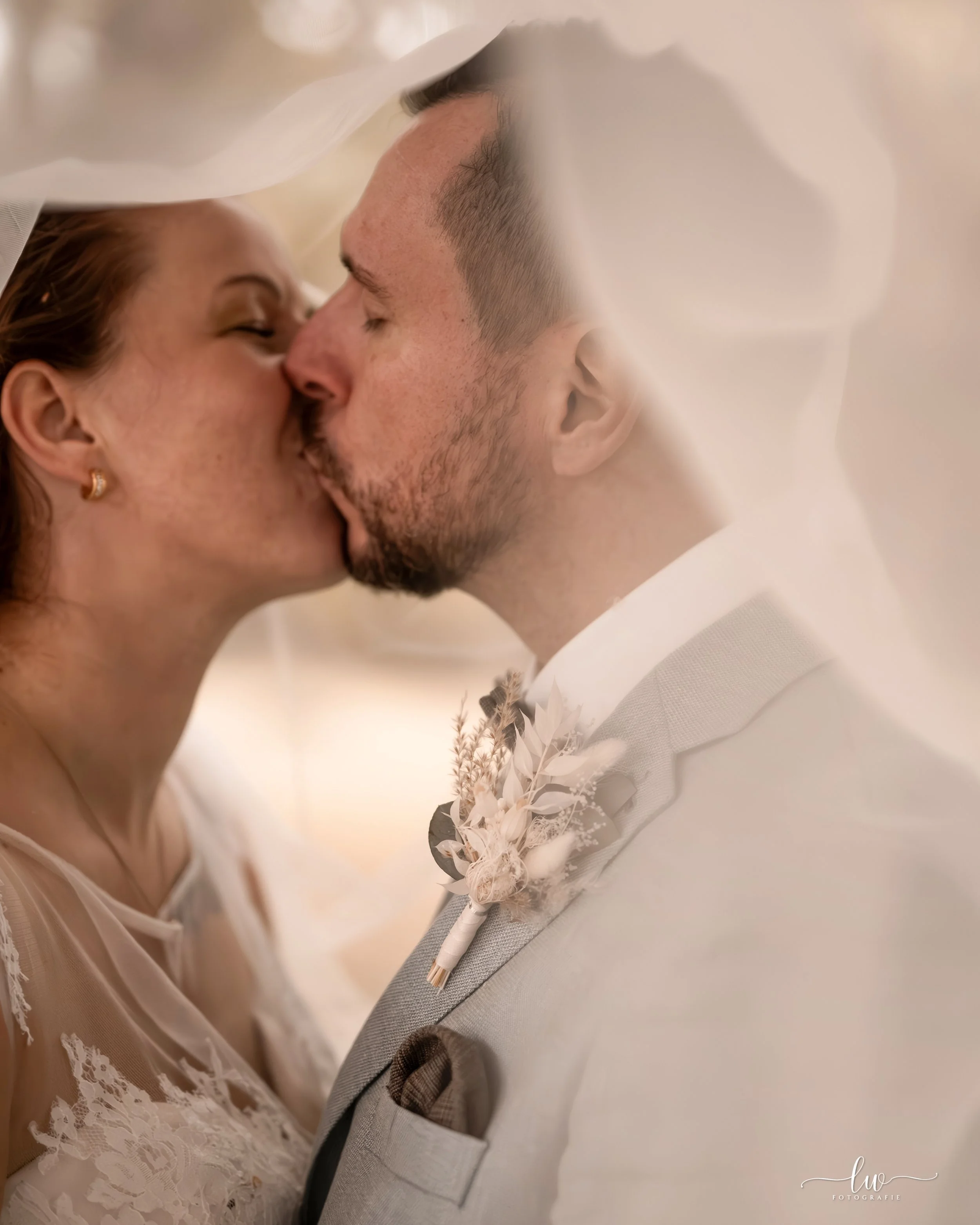 Ein Brautpaar in einer intimen Umarmung bei der Hochzeit, beide mit geschlossenem Blick, Nahaufnahme, romantische Atmosphäre, weiche Beleuchtung, elegante Kleidung, der Fokus auf den Gesichtern und dem Brautstrauß.