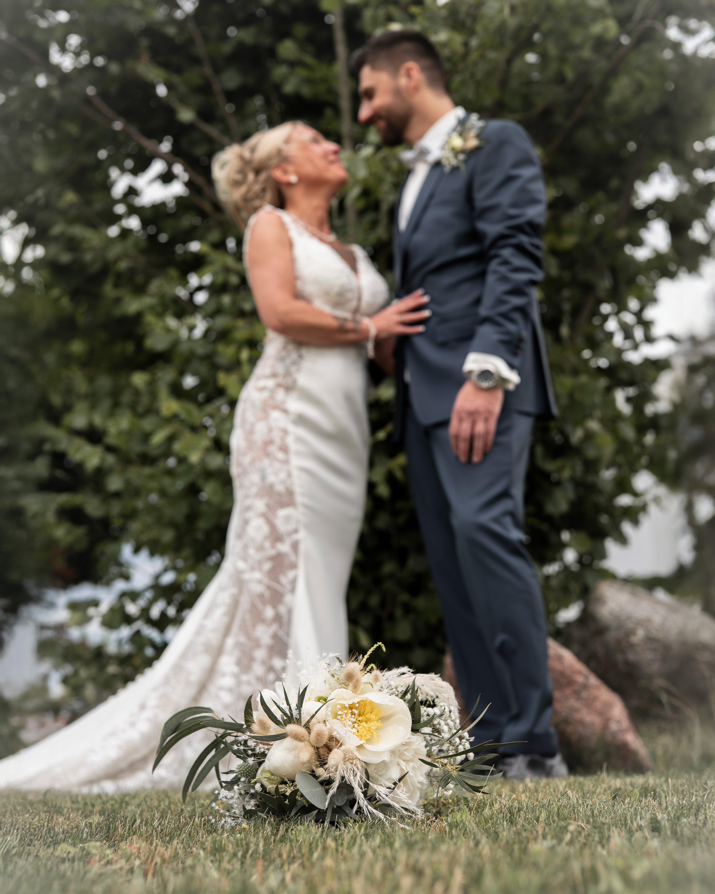 Verzäumte Braut und Bräutigam bei einer Hochzeit im Freien, Blick auf den Blumenstrauß auf dem Boden.
