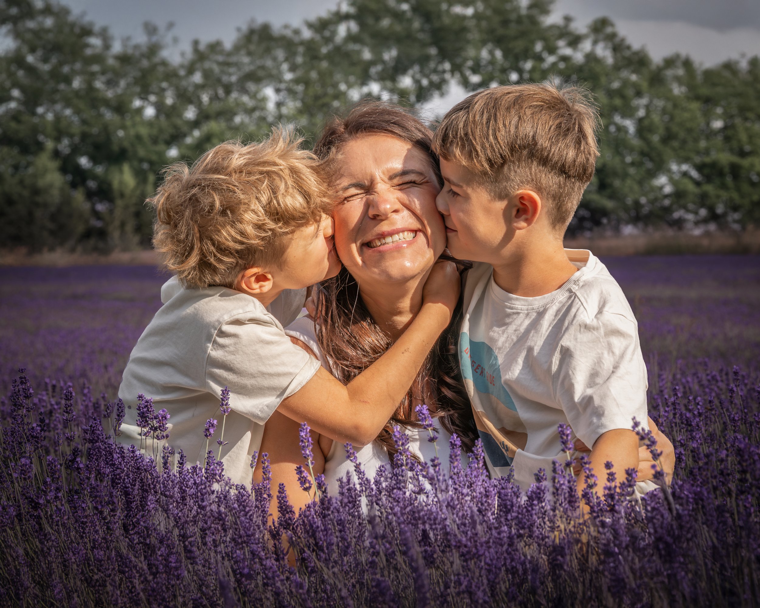 Eine Frau wird von zwei Jungen umarmt, während sie in einem Lavendel-Feld stehen, bei sonnigem Wetter.