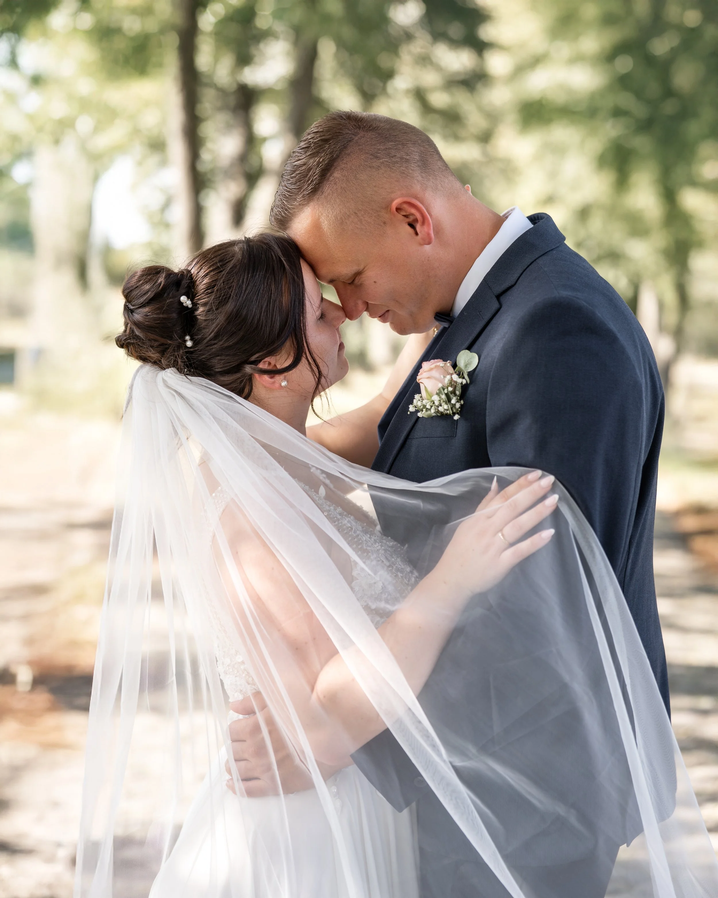 Ein Brautpaar, das sich bei ihrer Hochzeit im Freien umarmt, mit Nahaufnahme ihres Gesichtsausdrucks, umgeben von Bäumen und natürlicher Umgebung.