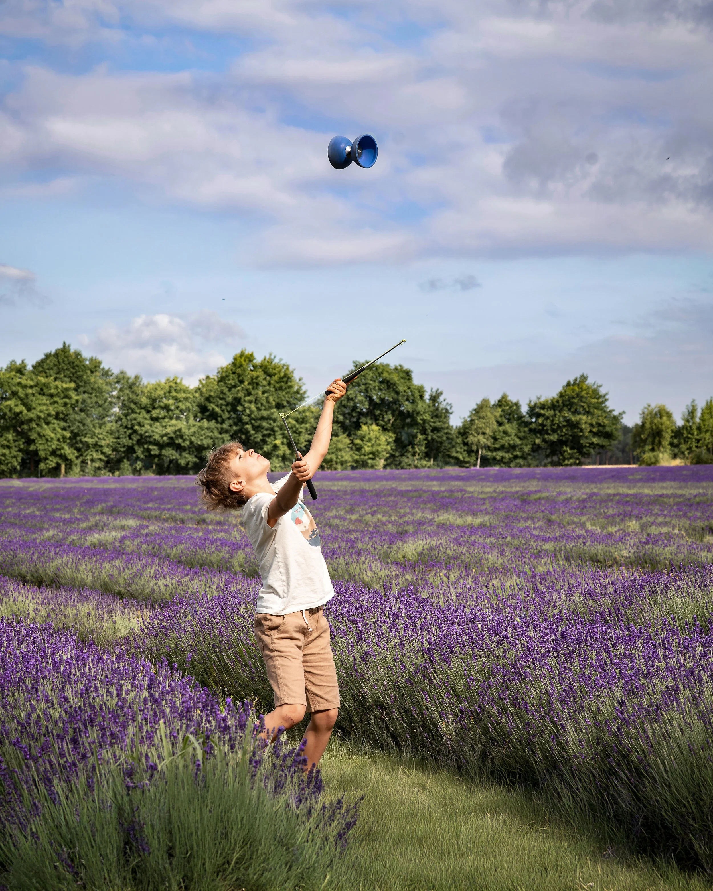 Ein Kind spielt mit einer Yoyo in einer Lavendelfeld mit Bäumen im Hintergrund, während die Wolken am Himmel vorbeiziehen.