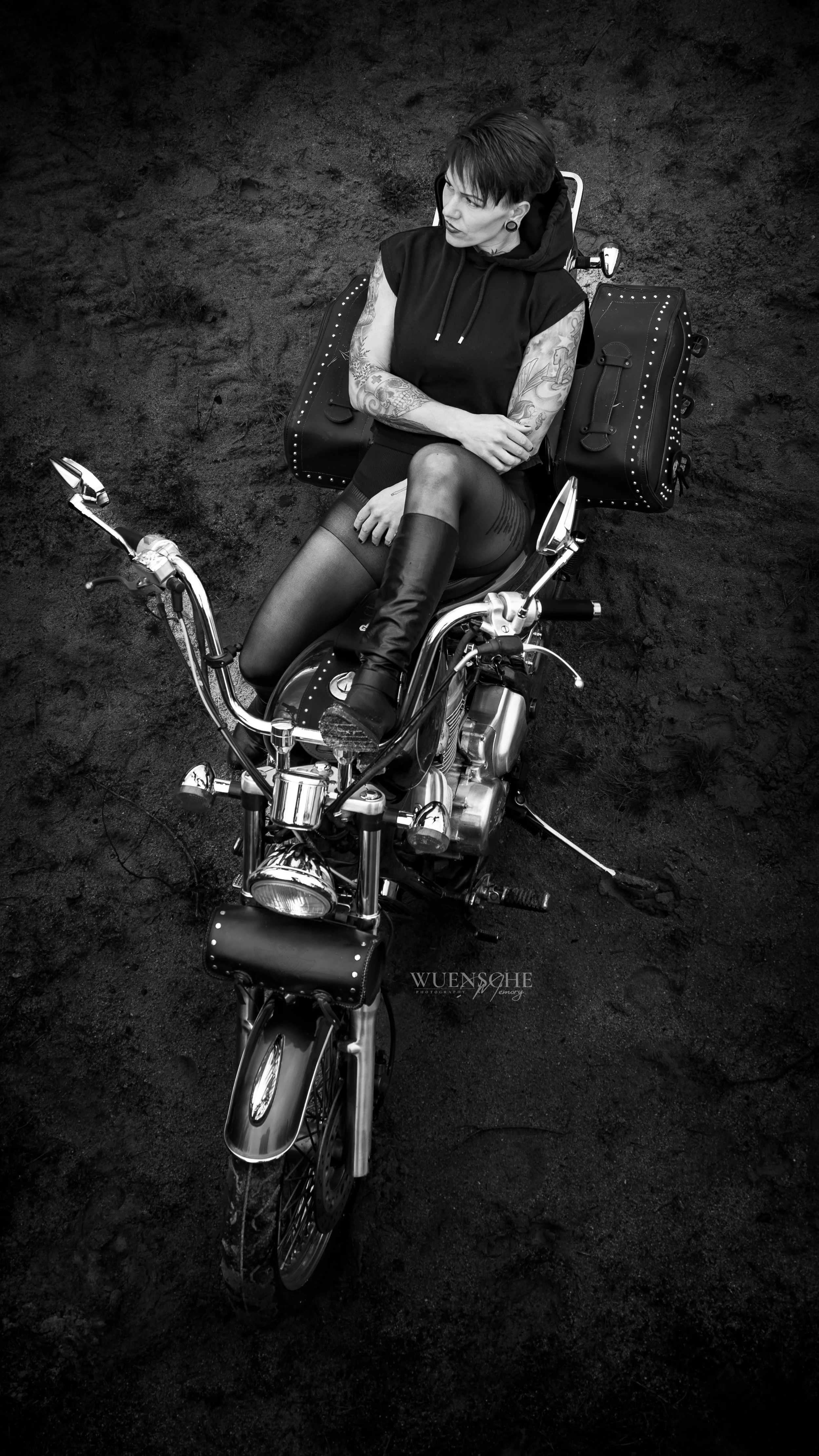 Schwarz-weiße Aufnahme eines Tattoos an einem arbeitenden Menschen, der auf einem Motorrad sitzt, mit dunklem Hintergrund.