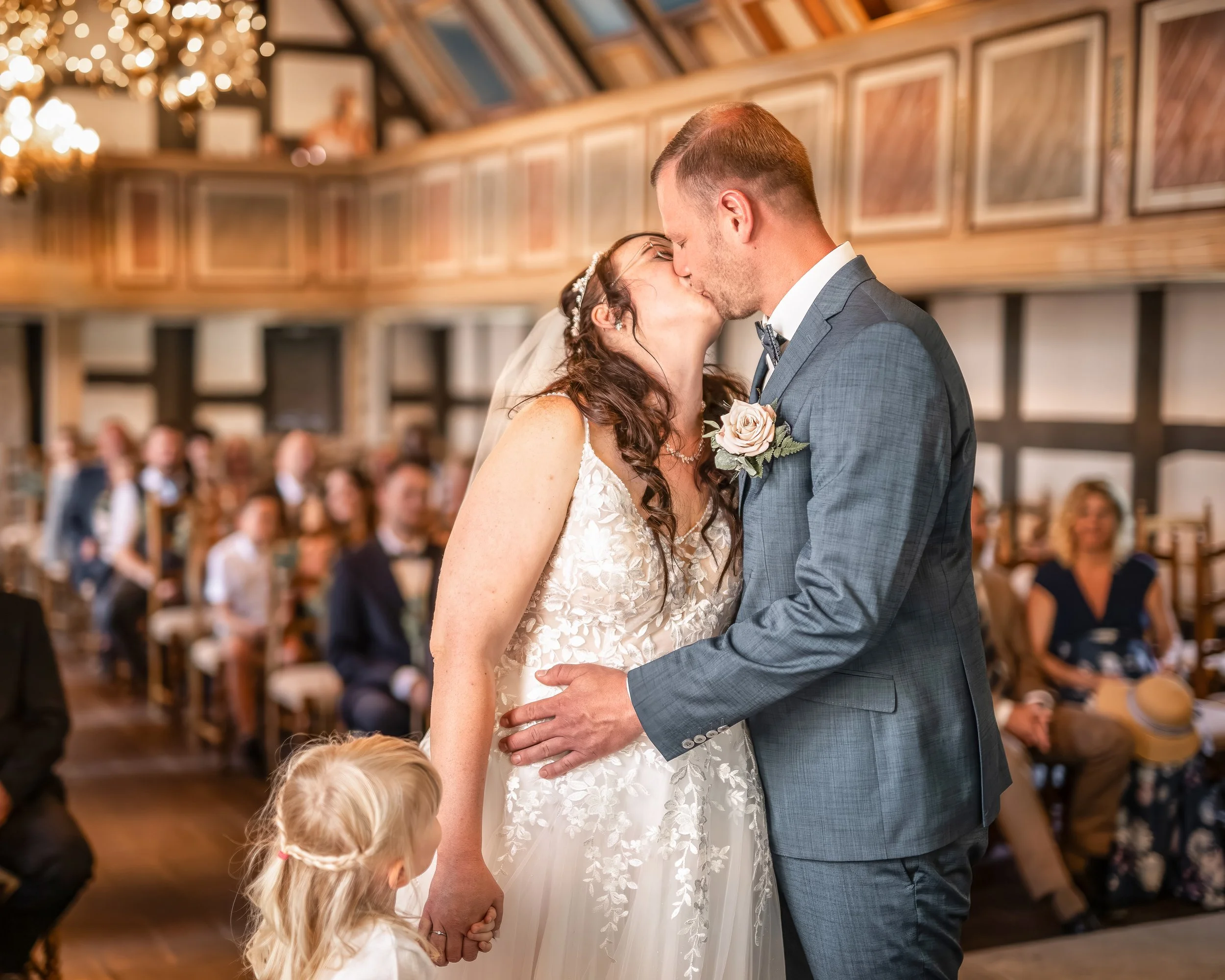 Das Brautpaar küsst sich bei ihrer Hochzeit vor einer versammelten Hochzeitsgesellschaft in einem festlich dekorierten Raum.