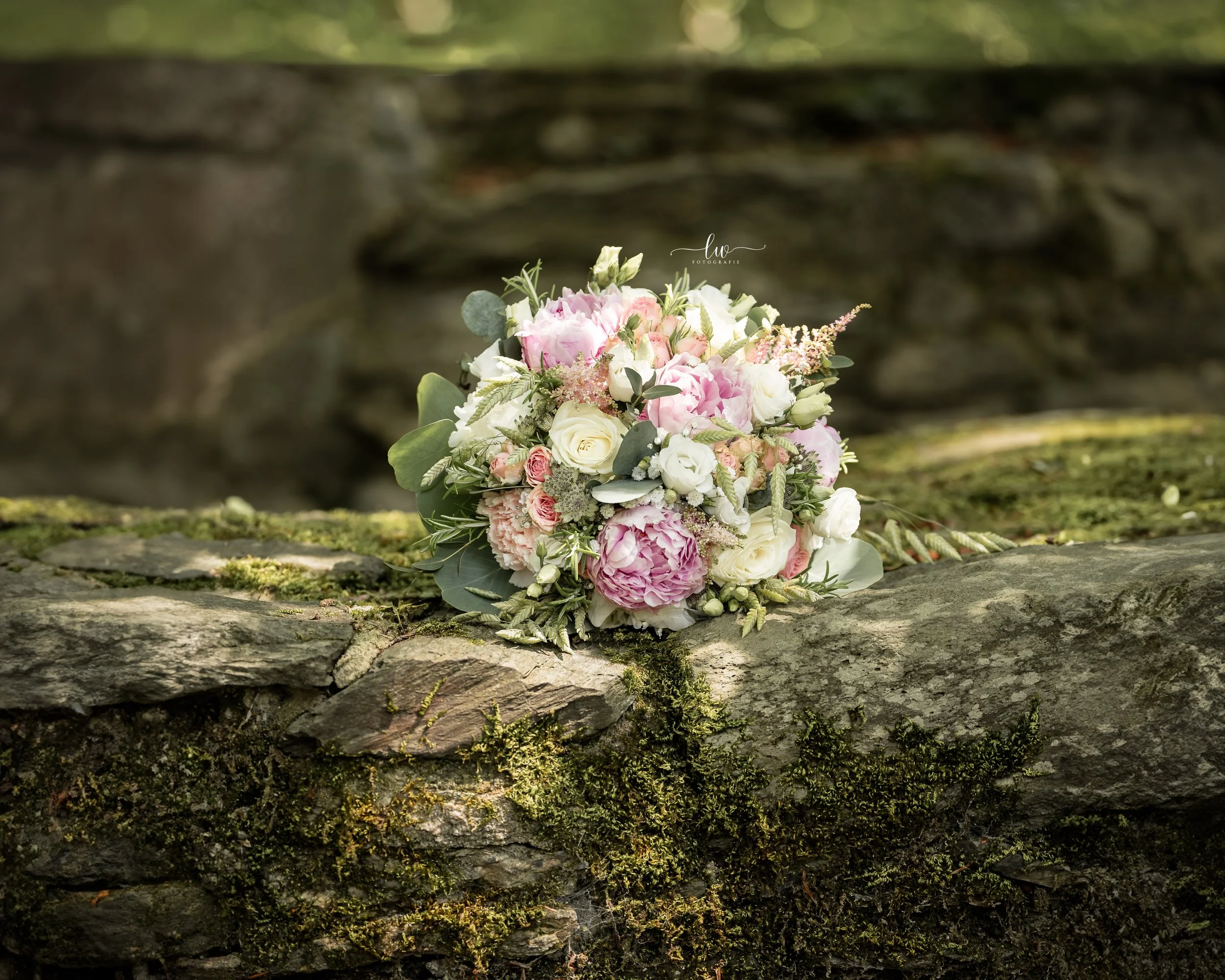 Blumenstrauß mit rosa und weißen Blumen, auf einem moosbedeckten Baumstamm in einem natürlichen Waldumfeld