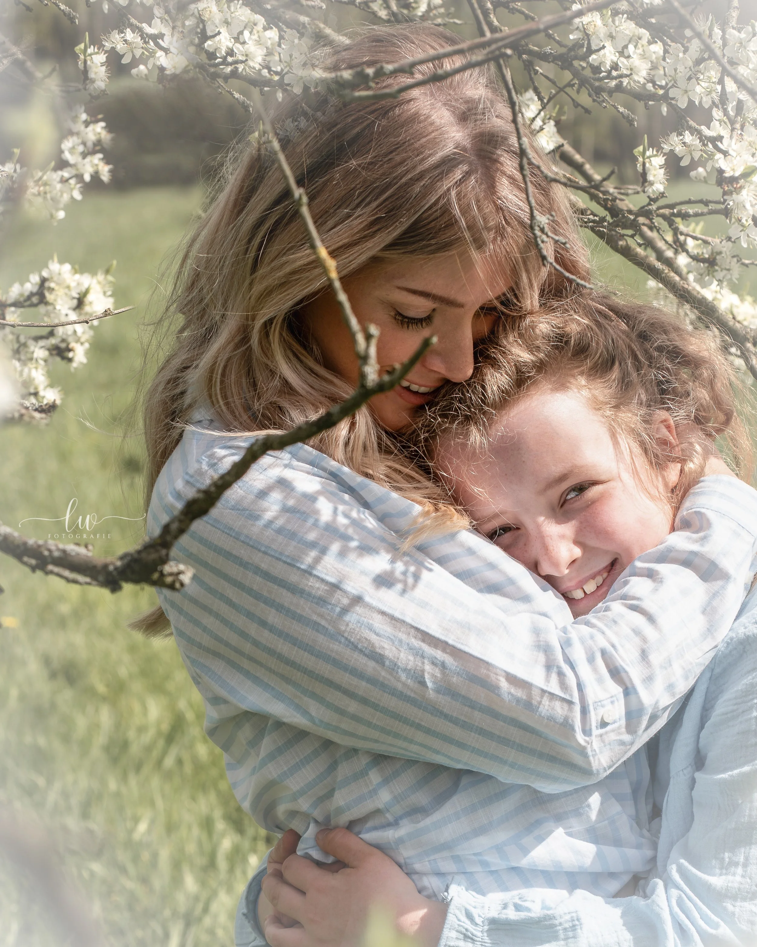 Zwei Frauen umarmen sich in einem blühenden Frühlingsgarten, lachend und glücklich.