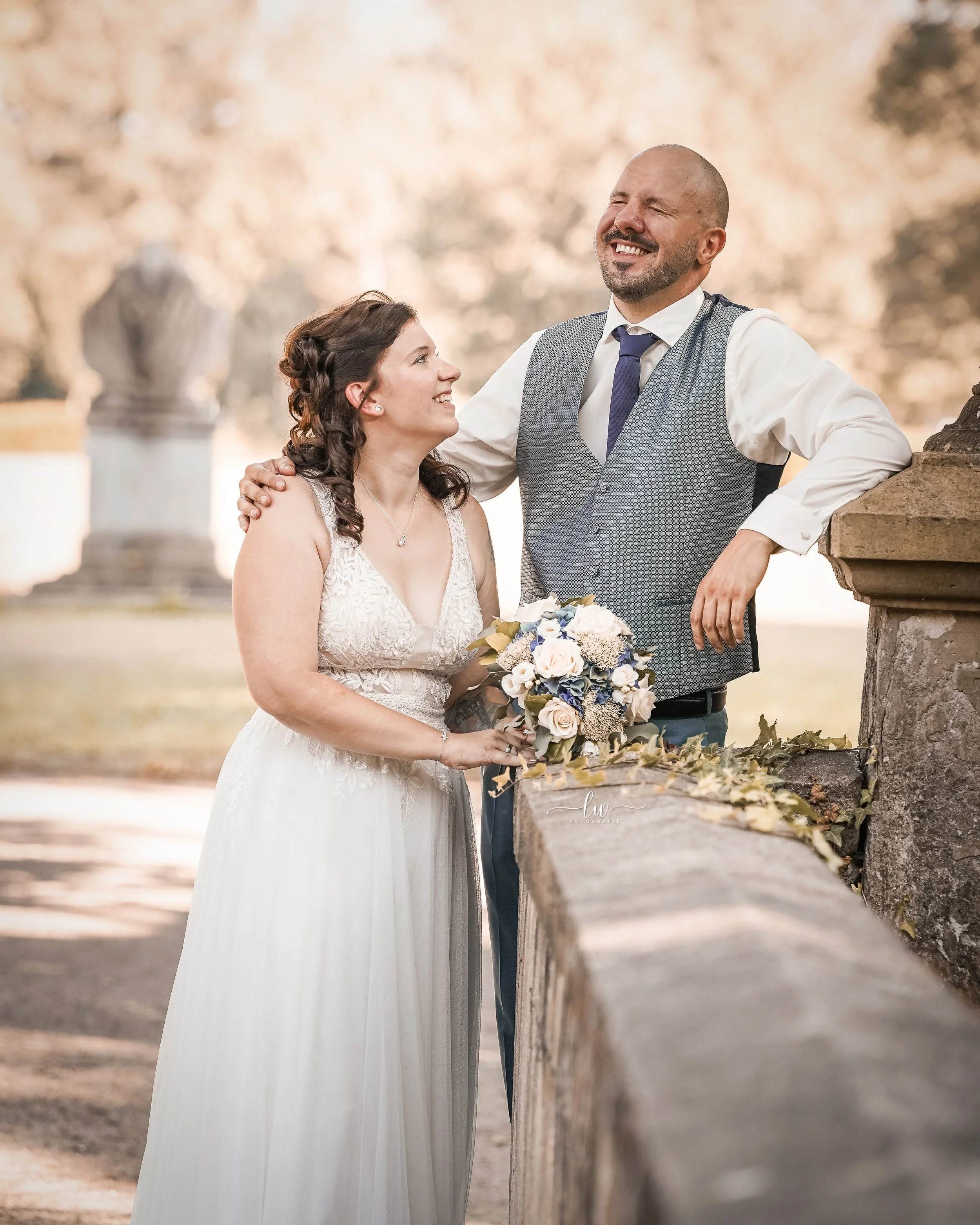 Ein Mann und eine Frau bei einer Hochzeit im Park, beide lächeln.