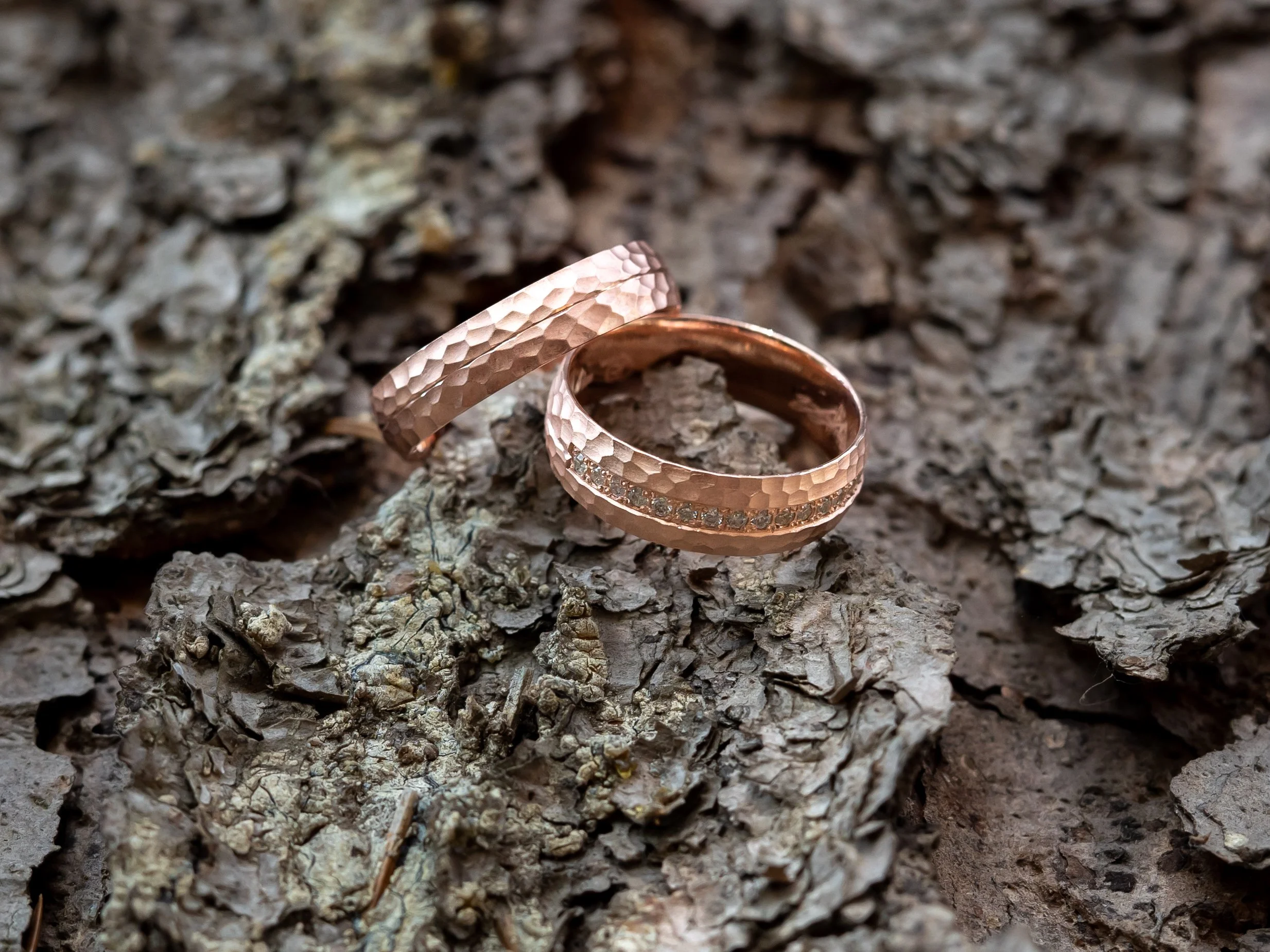 Zwei kupferne Ringe mit Hammerprägung liegen auf einer braunen, rissigen Baumrinde.