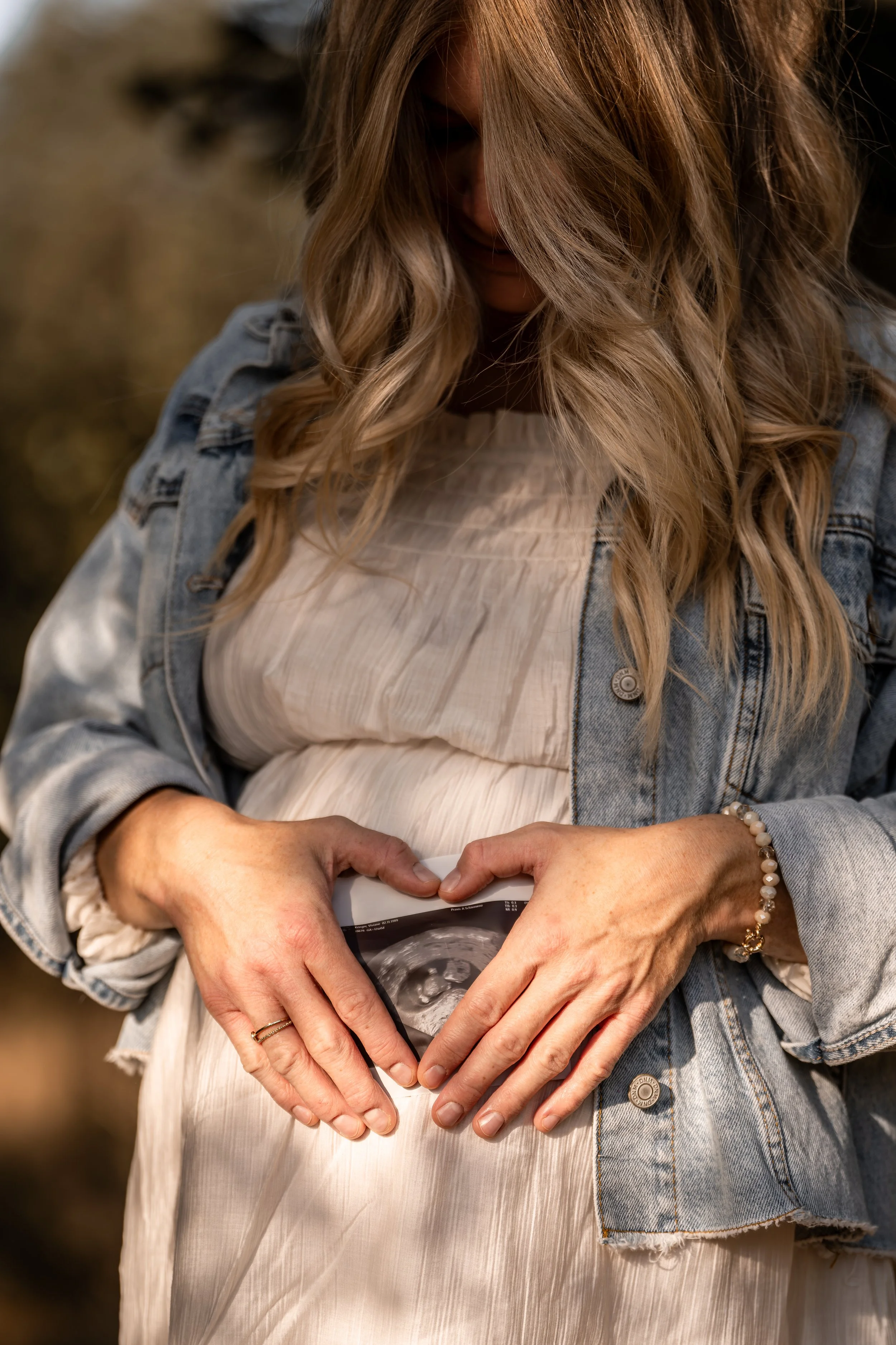 Eine schwangere Frau hält ein Ultraschallbild ihres Babys vor ihrem Babybauch und bildet damit ein Herz.