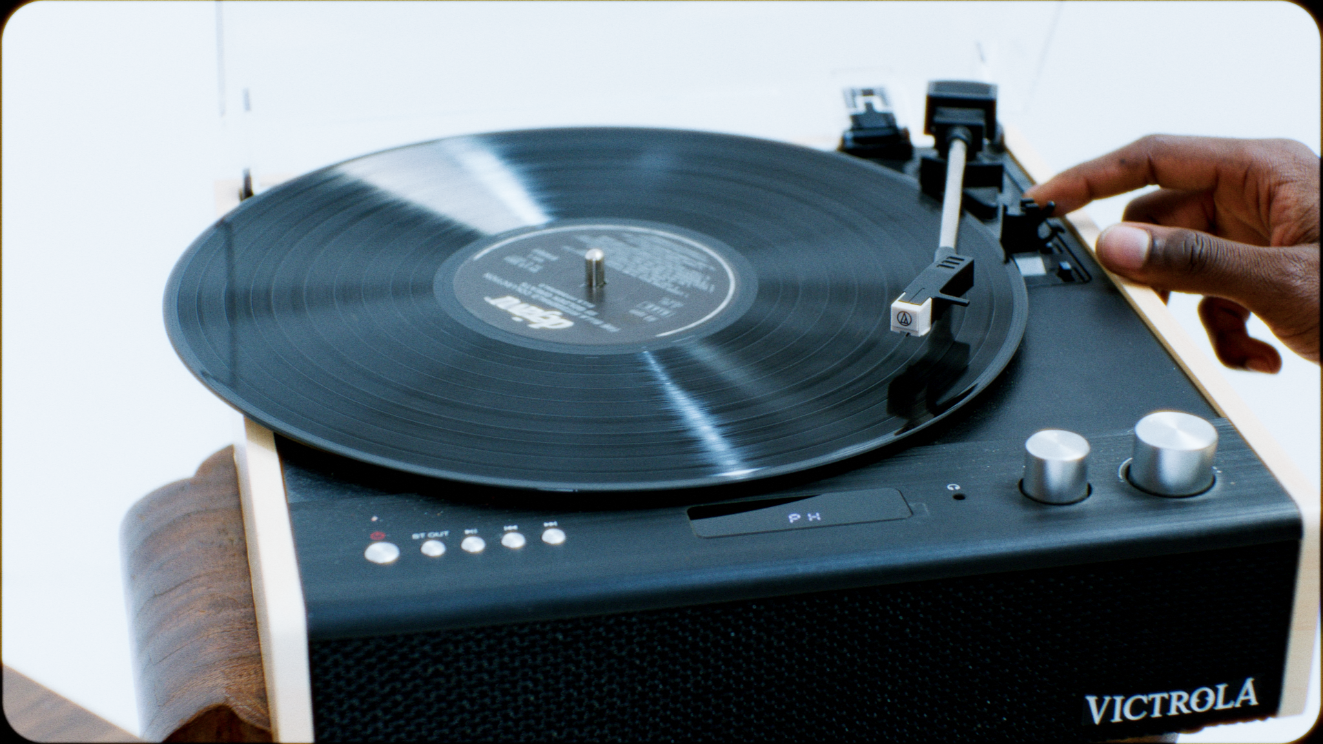 A person adjusting the tonearm of a black vinyl record player on a wooden stand.