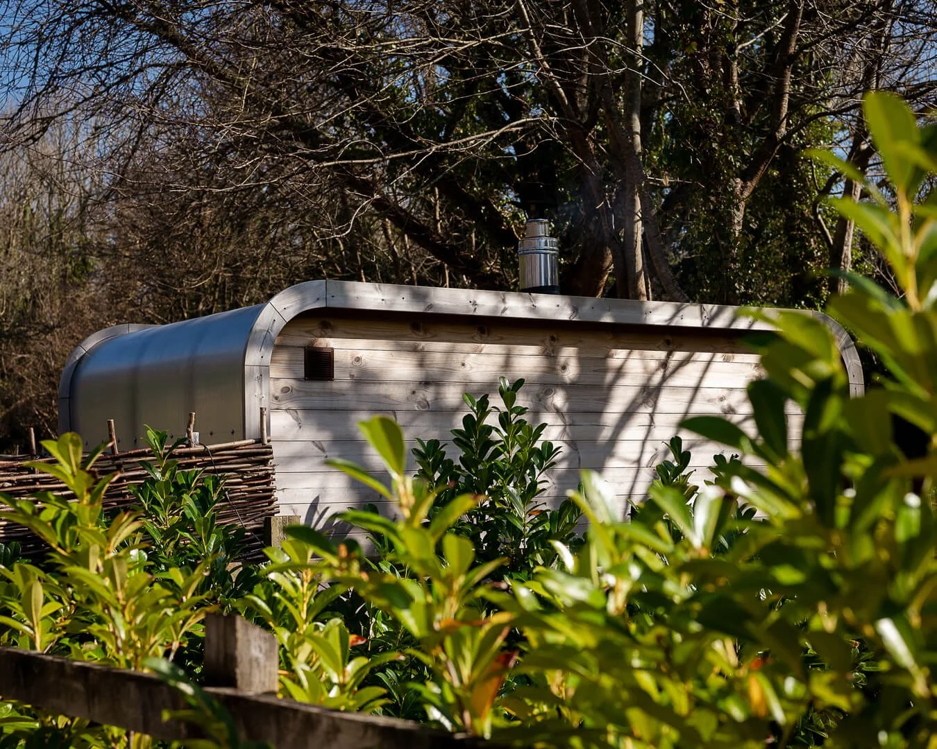 The back of the wood fired sauna at Melancoose woodland spa surrounded by shrubs and trees