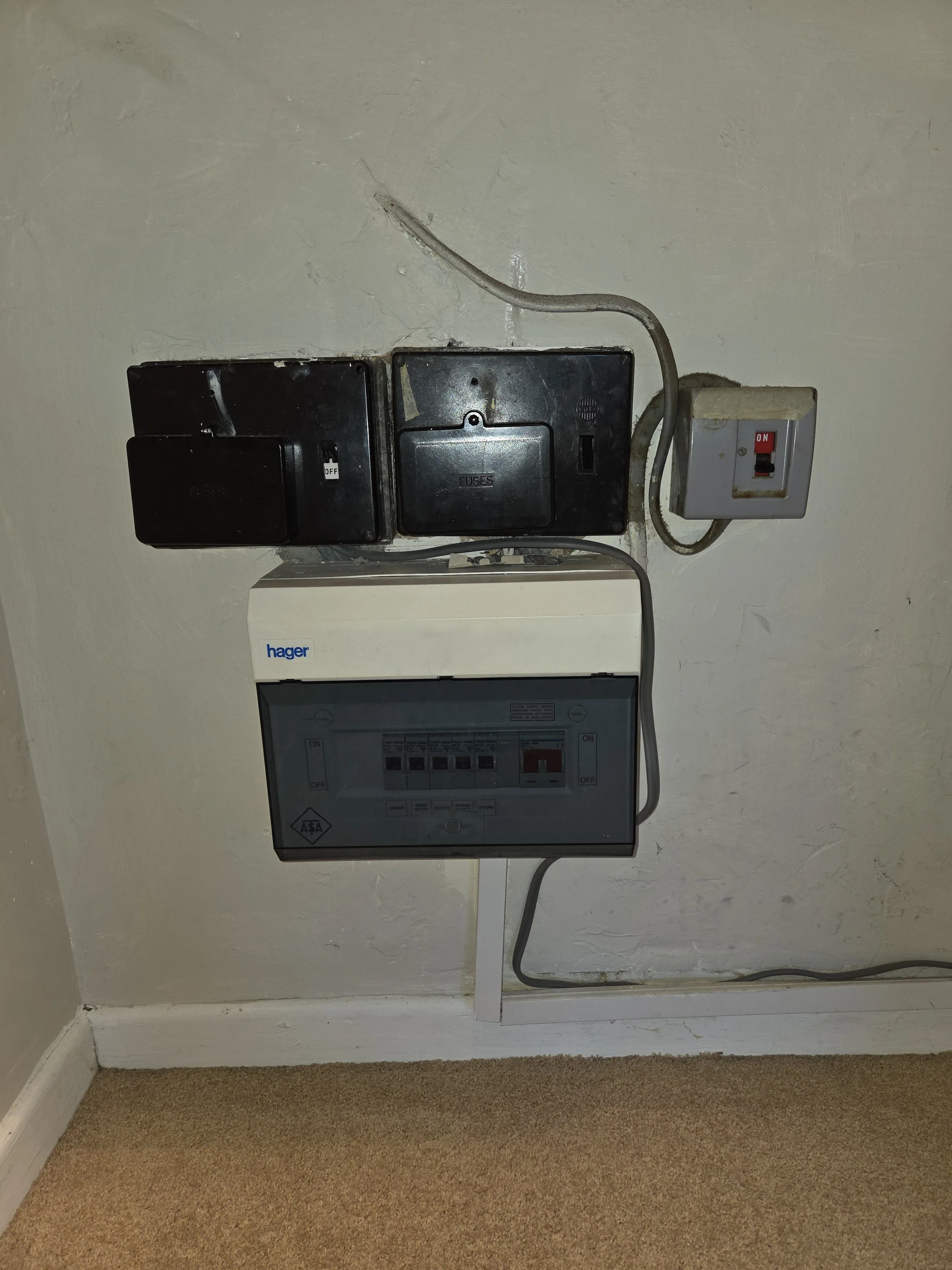 Electrical meters and switches on a wall with visible wiring and a beige carpeted floor.