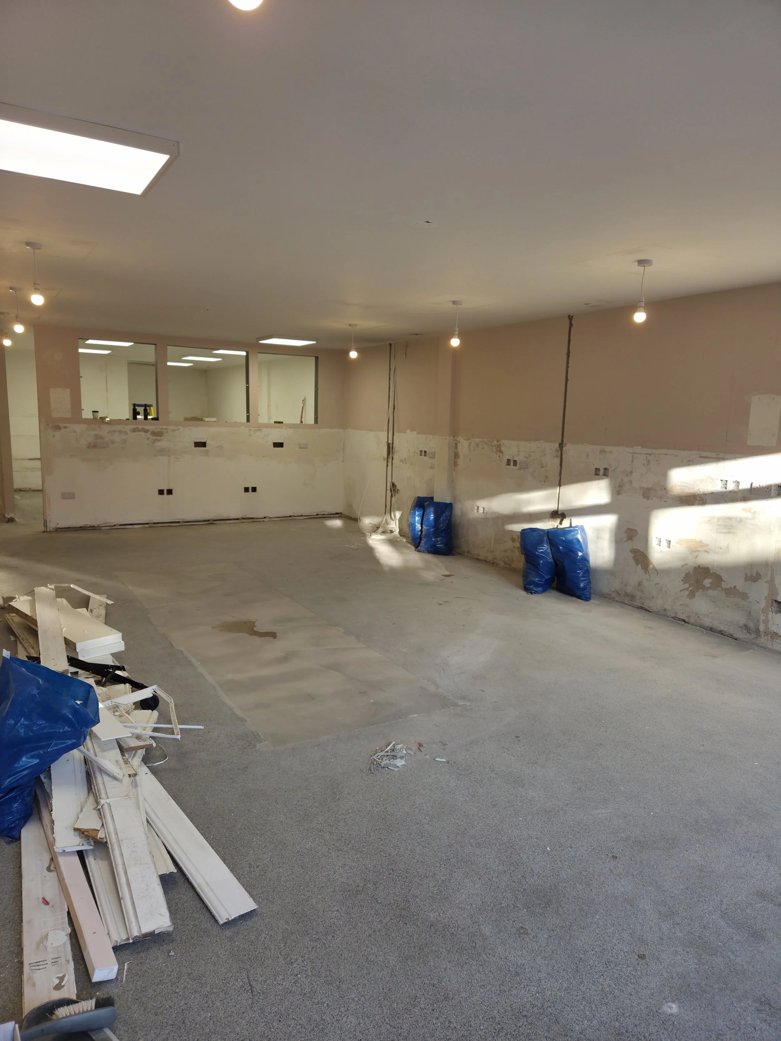 Interior of a room under renovation with exposed walls, uneven flooring, and construction debris, including blue plastic bags, scattered around.