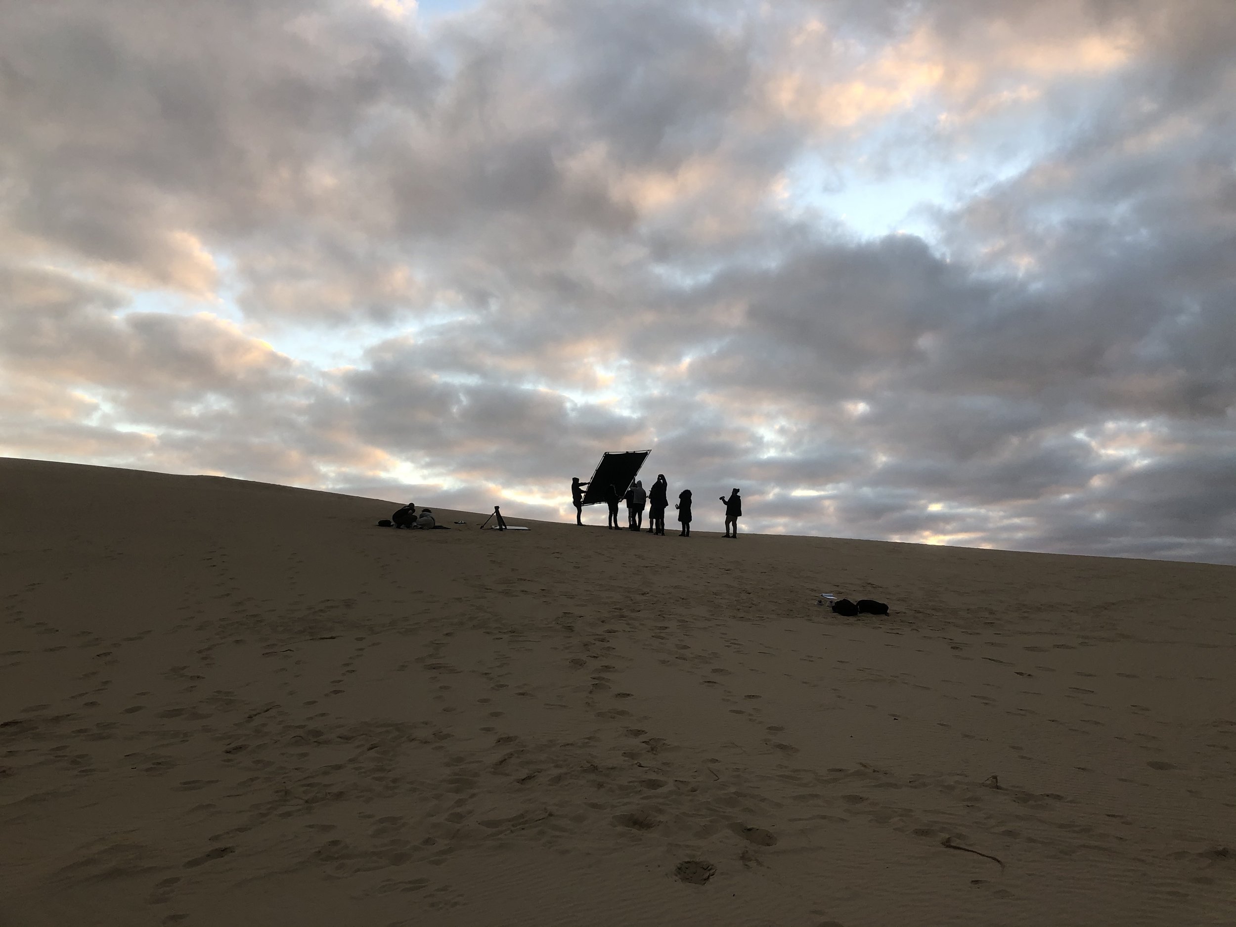 Silhouettes of people on a sand dune under a cloudy sky.