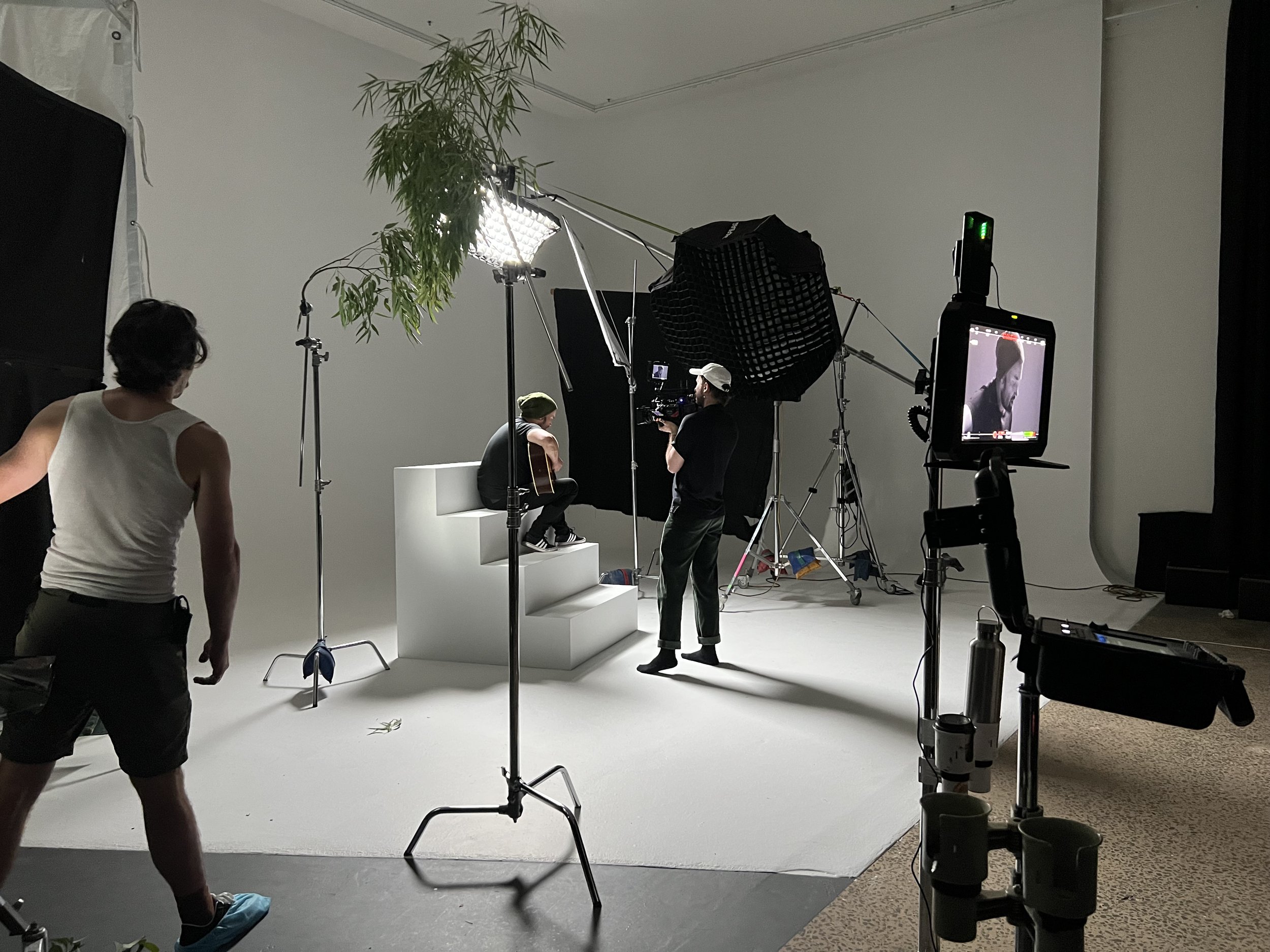 Photography studio setup with subject on white platform and crew adjusting lighting equipment
