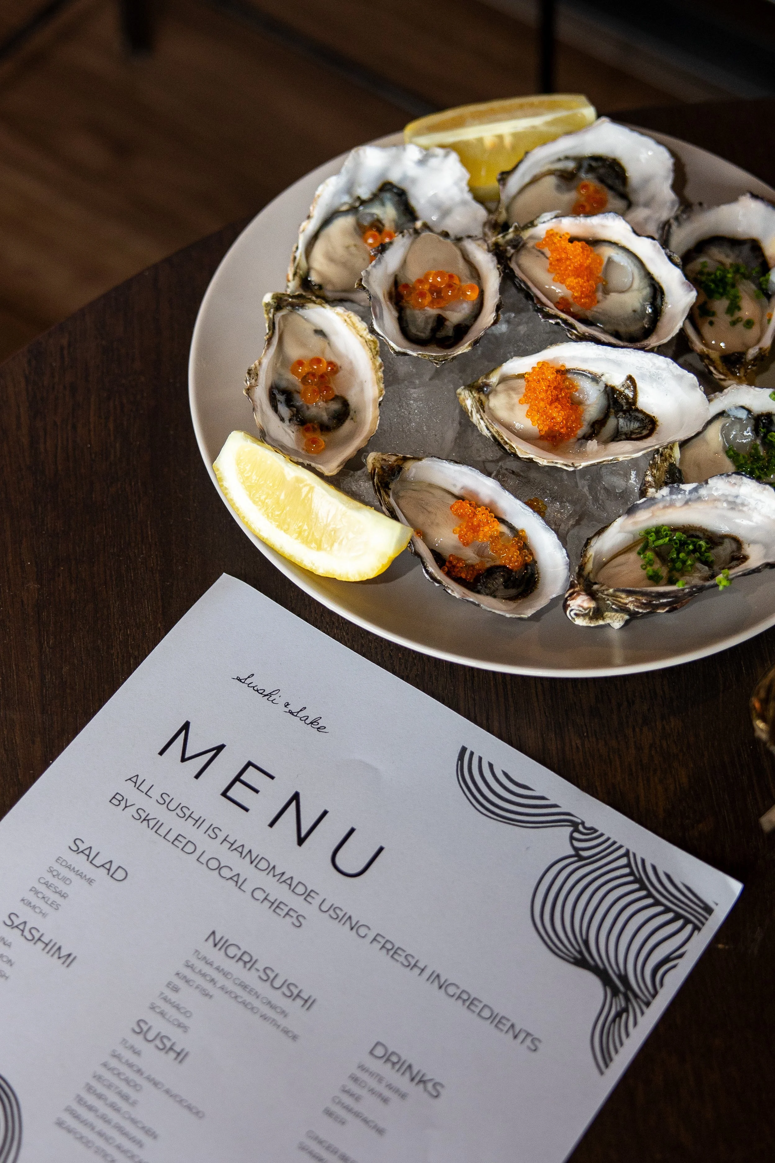 A white plate with several raw oysters topped with orange fish roe and garnished with lemon wedges, placed on ice.