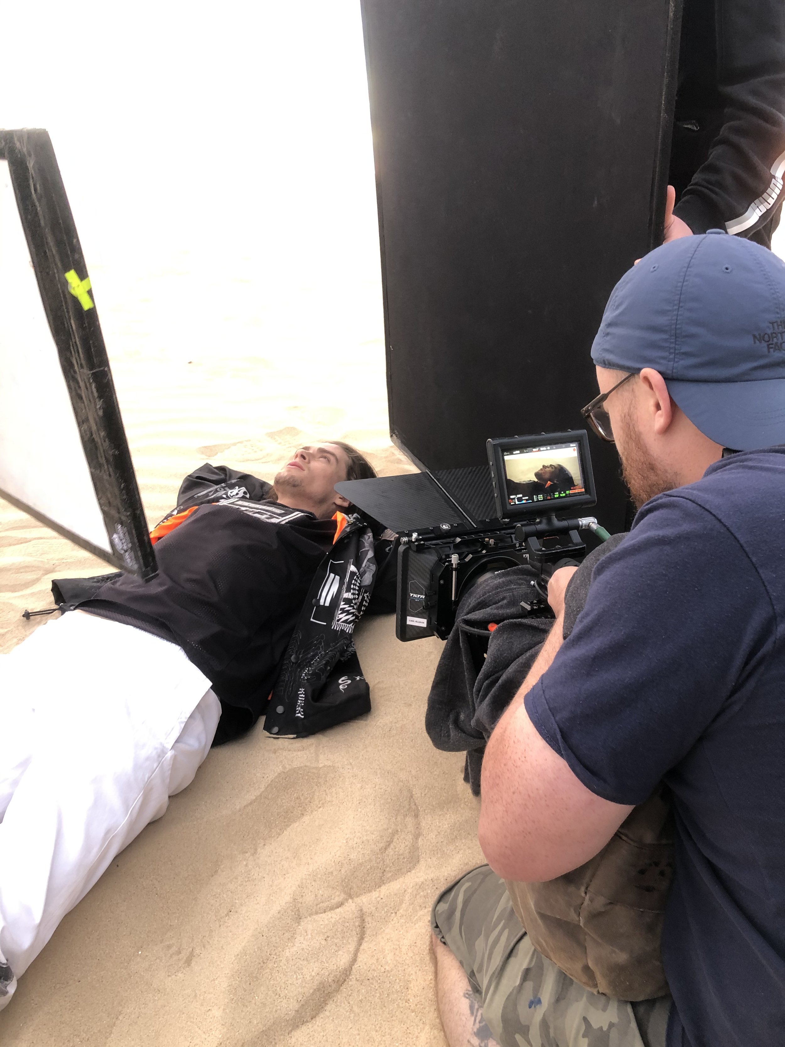 Person lying on sand while being filmed by a camera operator