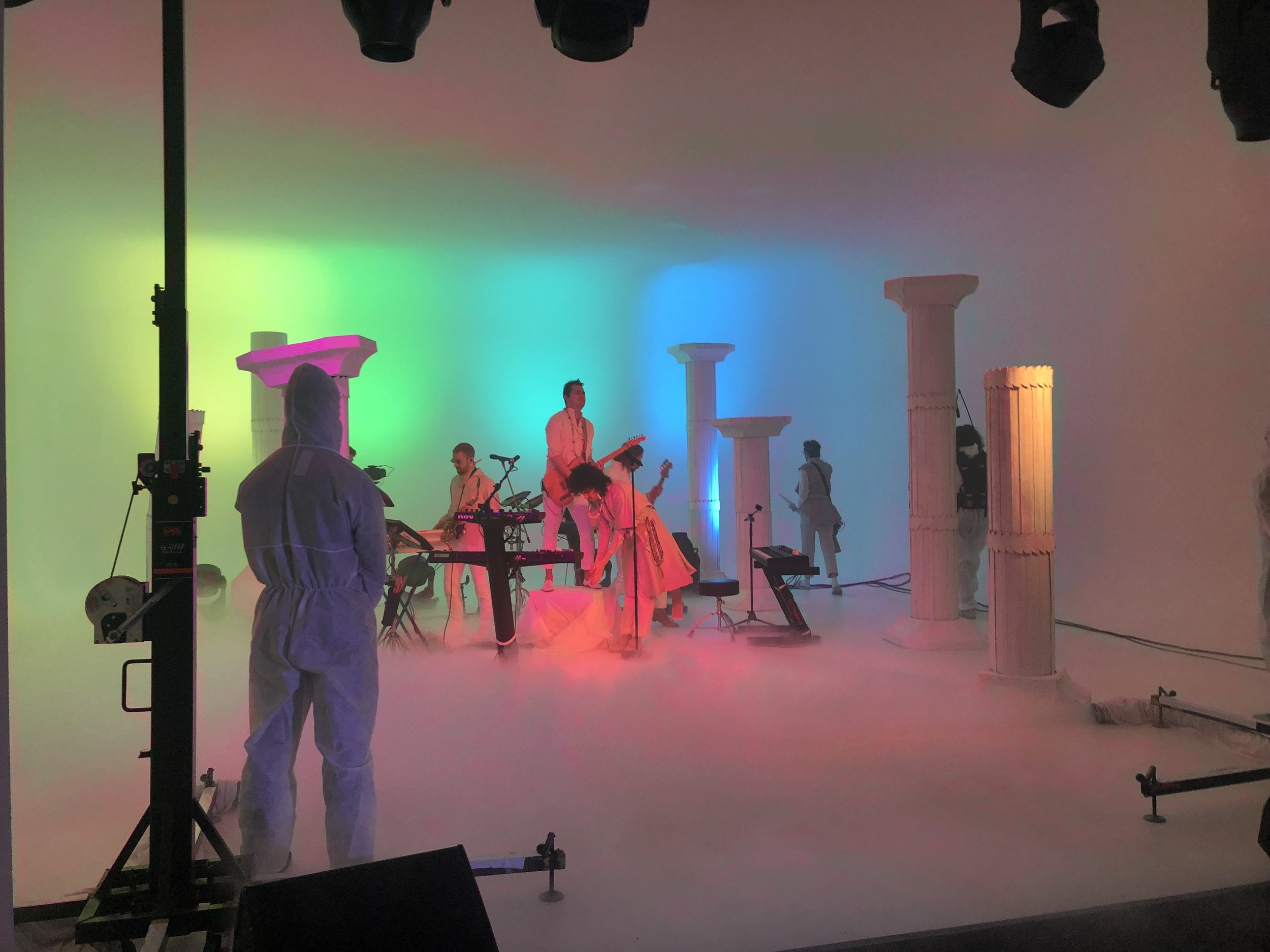 A colorful stage setup with musicians in costumes playing instruments among tall columns and dramatic lighting effects.