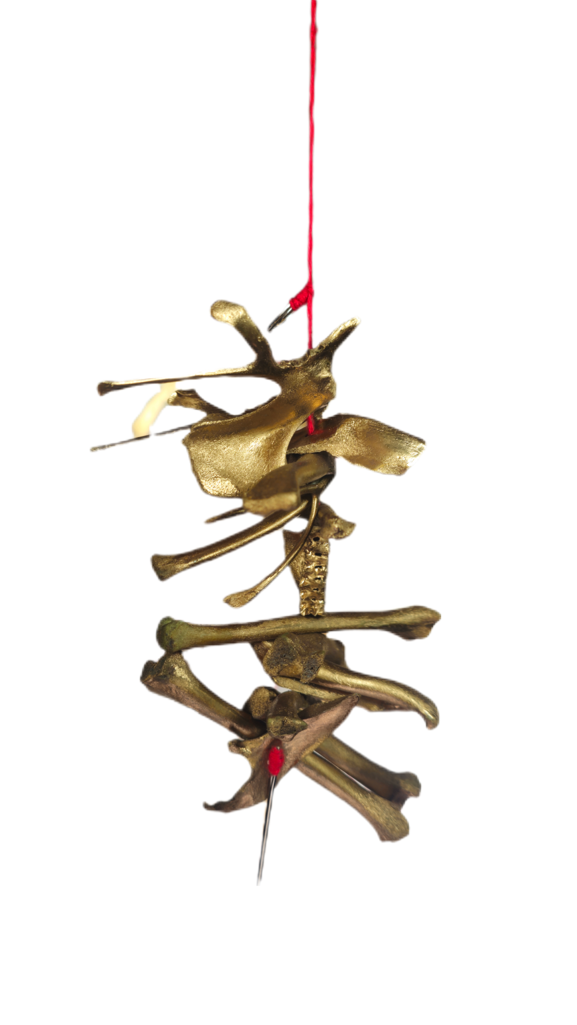 A decorative hanging sculpture made of various gold-colored metallic bones, beads, and small objects, tied together with red string, against a black background.
