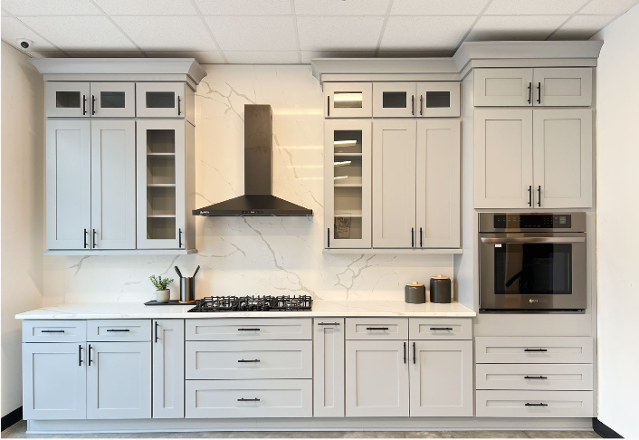 Modern kitchen with white cabinetry, marble backsplash, stainless steel oven, gas stove, black range hood, and decorative items on the counter.