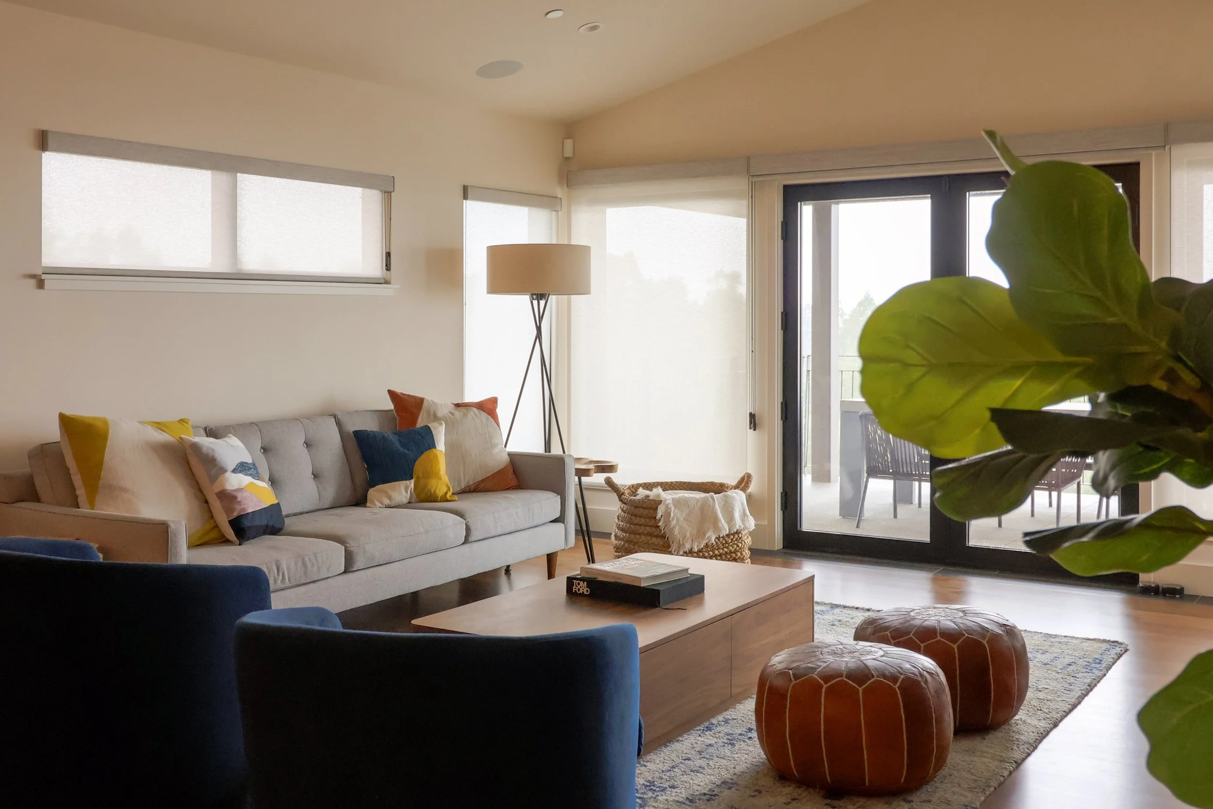 A living room with blue swivel chairs, a walnut coffee table, leather poufs, grey sofa.