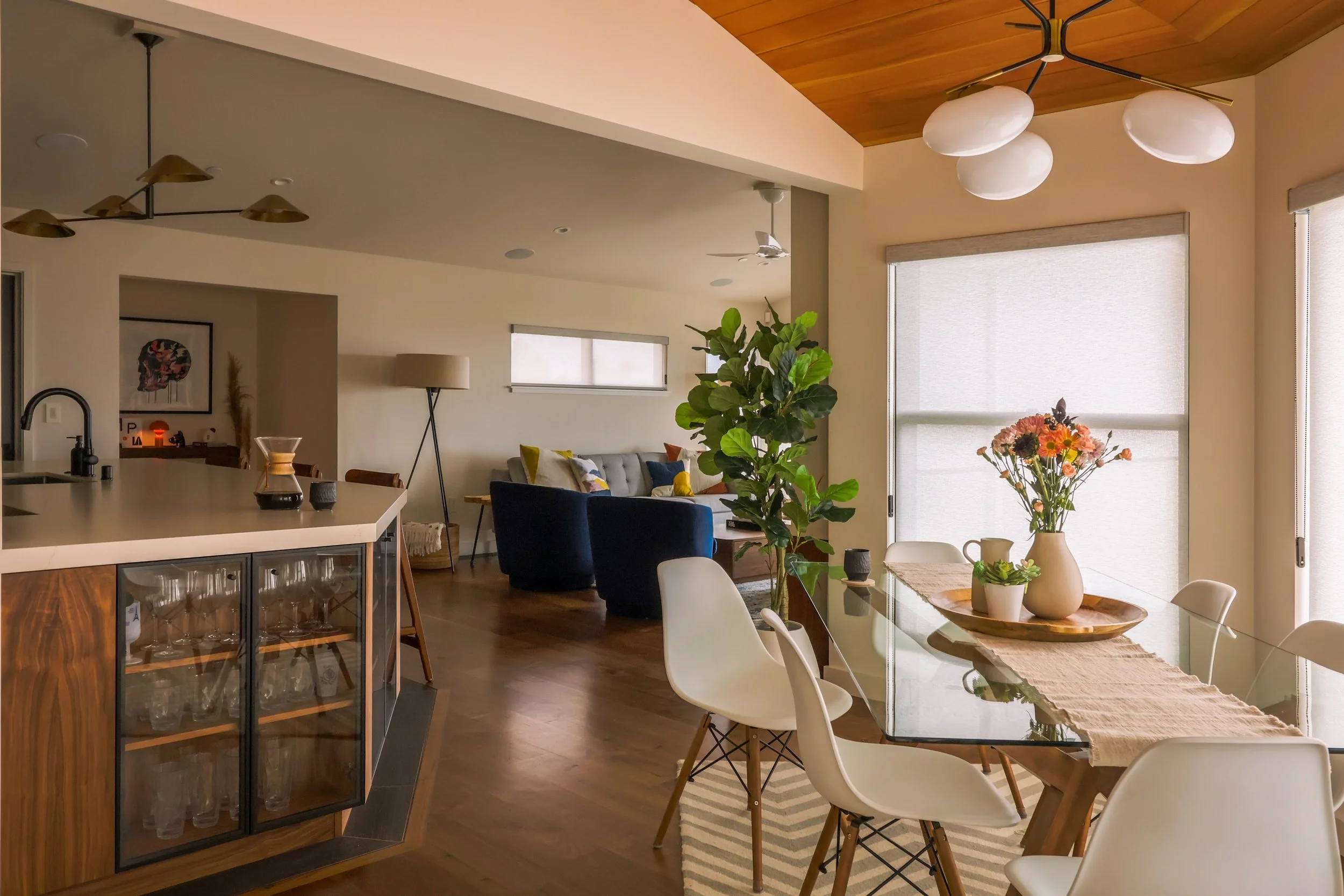 Breakfast nook with white chairs and a floral arrangement on the table. The living room and kitchen are visible in the background, a chemex with coffee inside sits on the kitchen counter.