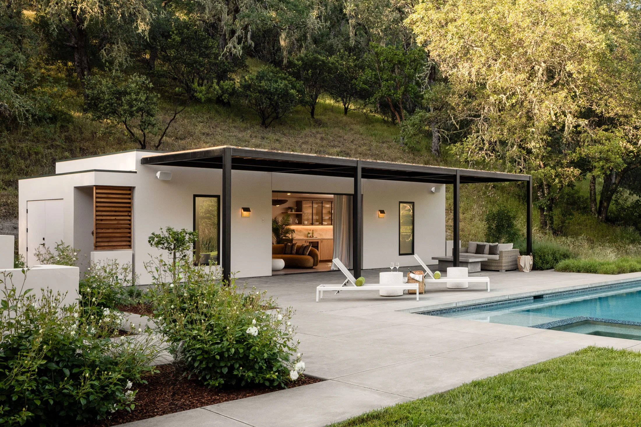 Contemporary house with open living area, outdoor patio, swimming pool, surrounded by greenery and trees.