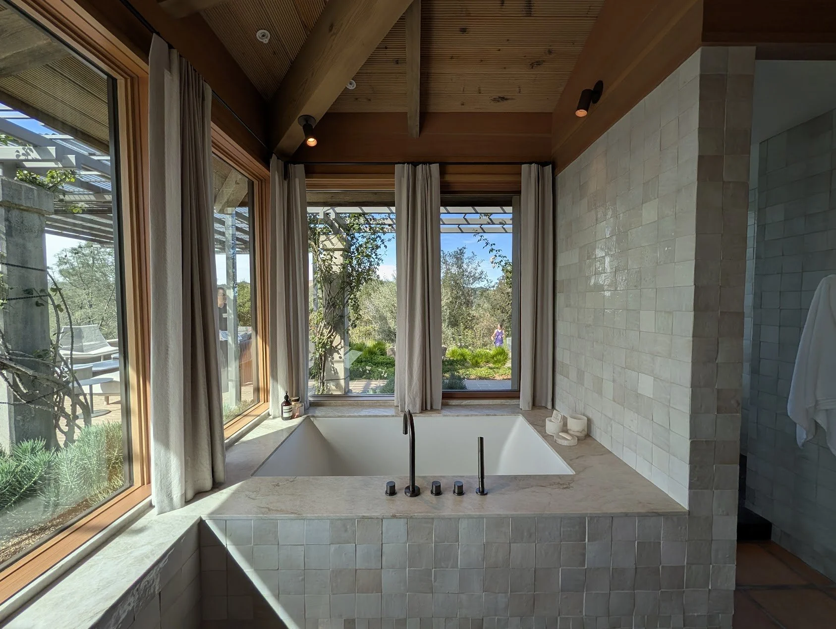 A bathroom fitted with zellige tiles on all walls, large windows look out into the yard from the bath tub.
