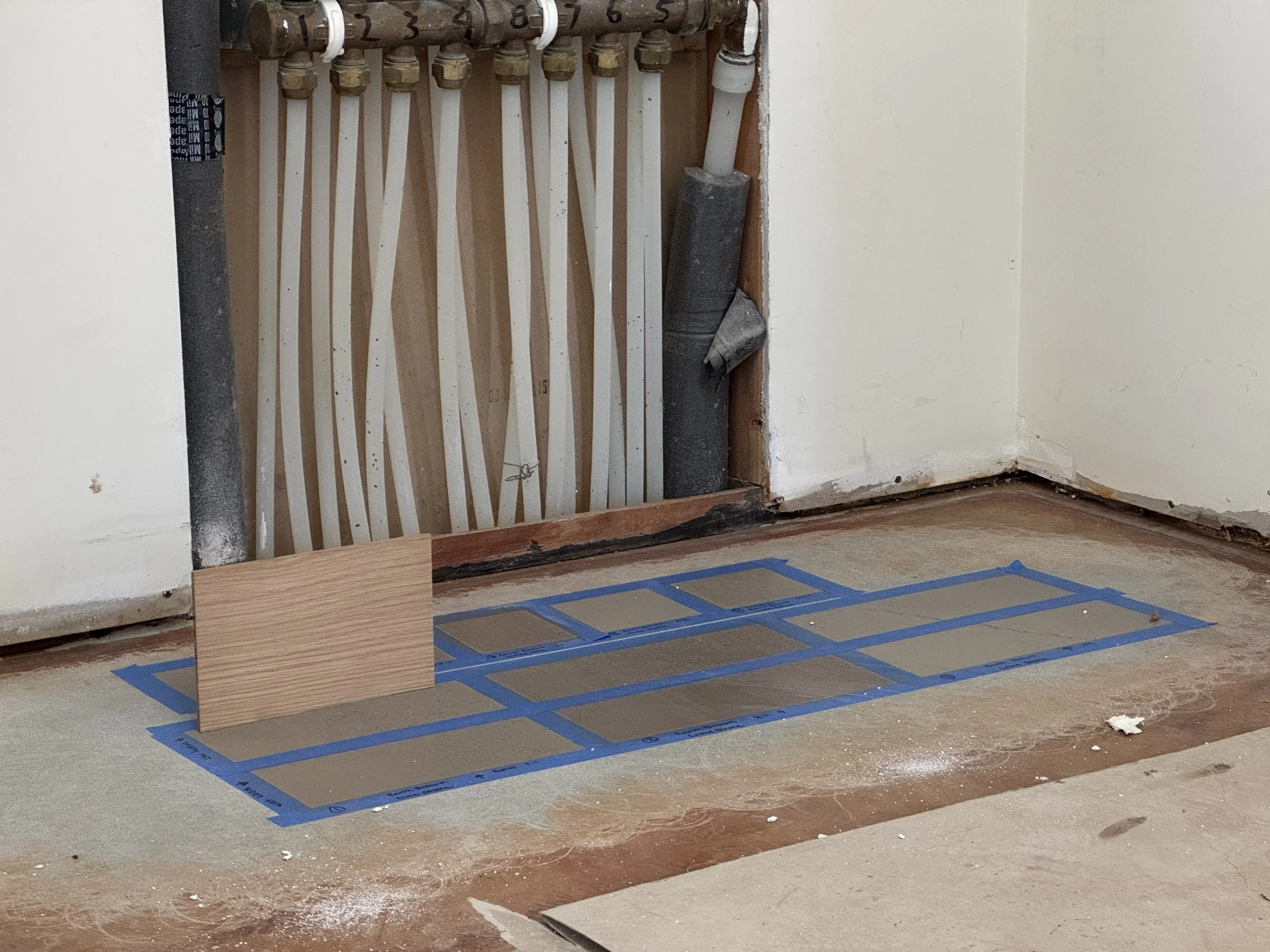 Open drywall section showing a manifold of water pipes, a concrete floor with masked areas for stain samples.