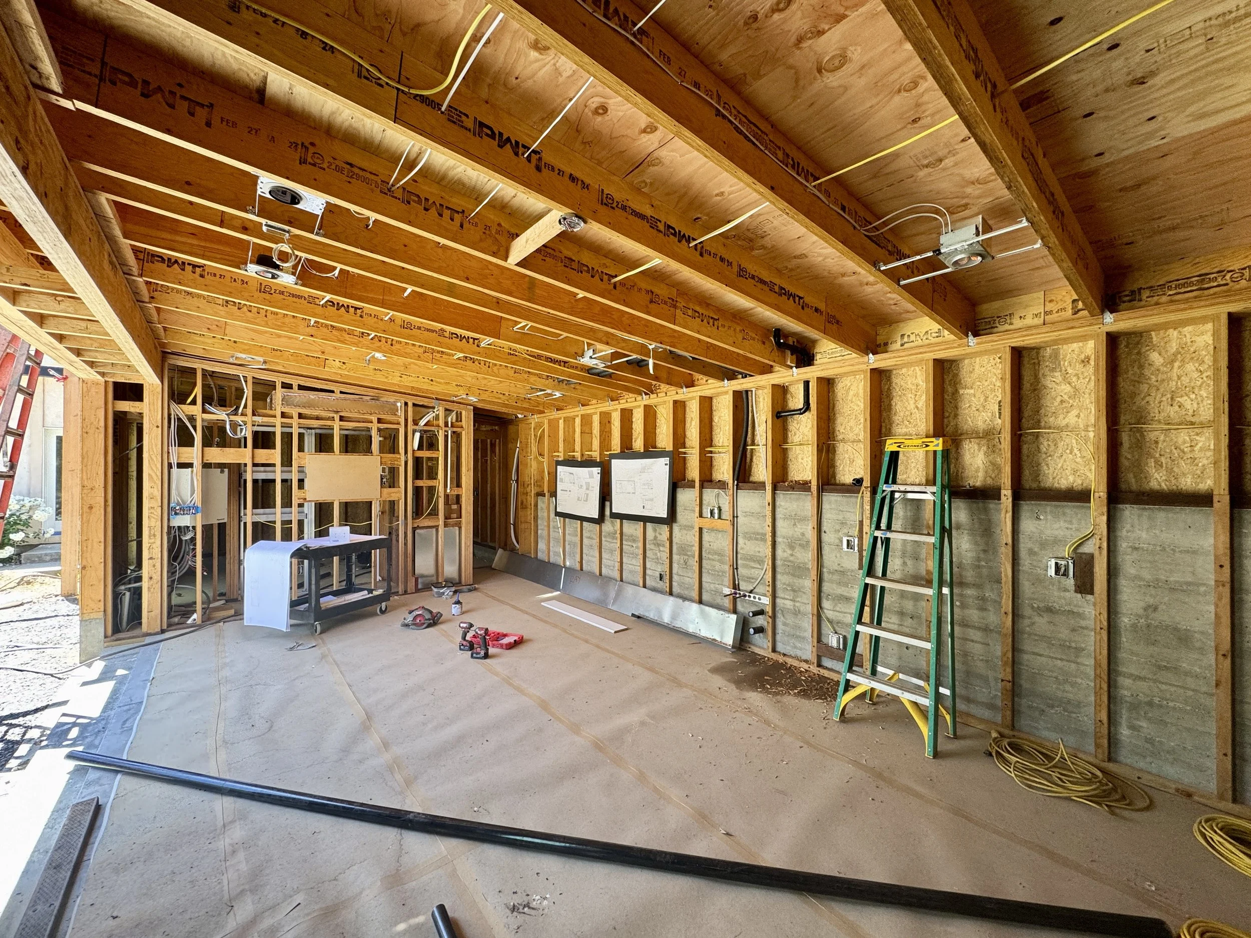 The interior of a new build poolhouse under construction, exposed framing show the runs of wires and pipes.