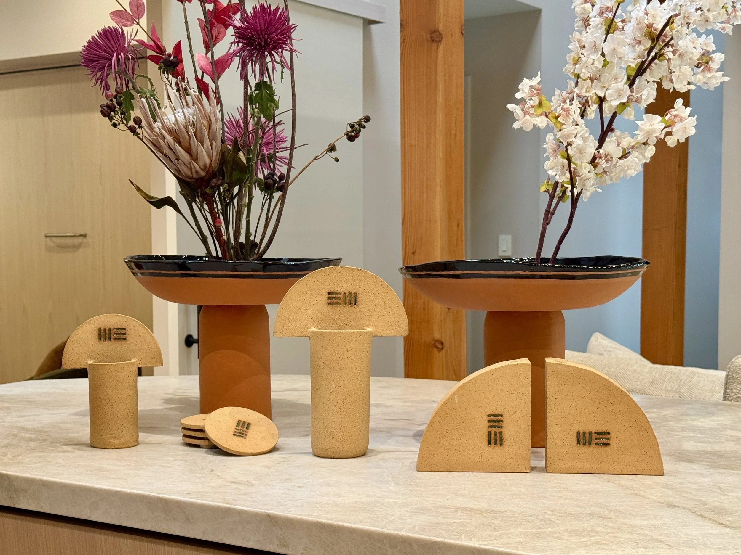 Bespoke ceramics sit on a countertop in the finished home, two large terracotta vases with black rims sit behind smaller vases and objects in a tan speckled clay color.